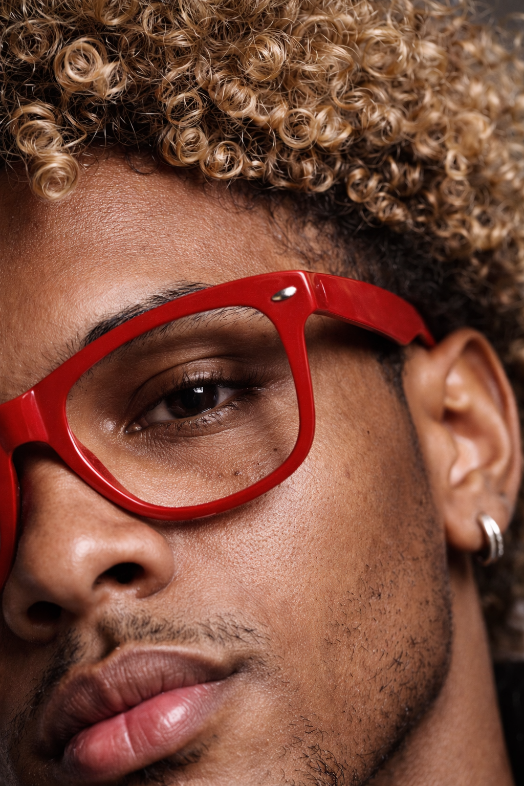 Close-up of a person wearing red glasses with curly hair and a hoop earring visible on one ear, showing part of the face from the nose to the forehead.