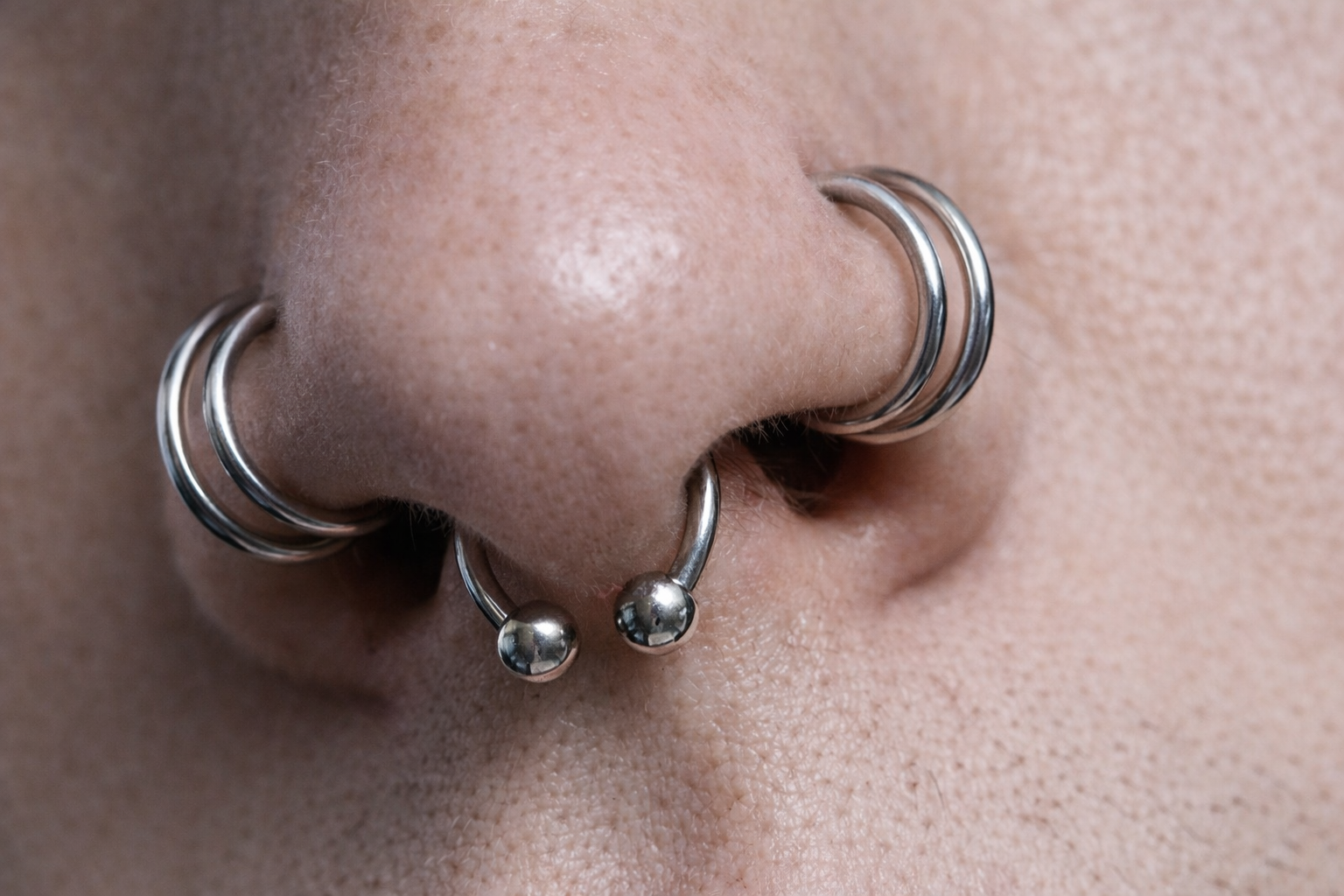 Close-up of a person's nose with multiple silver hoop and captive ring nose piercings.
