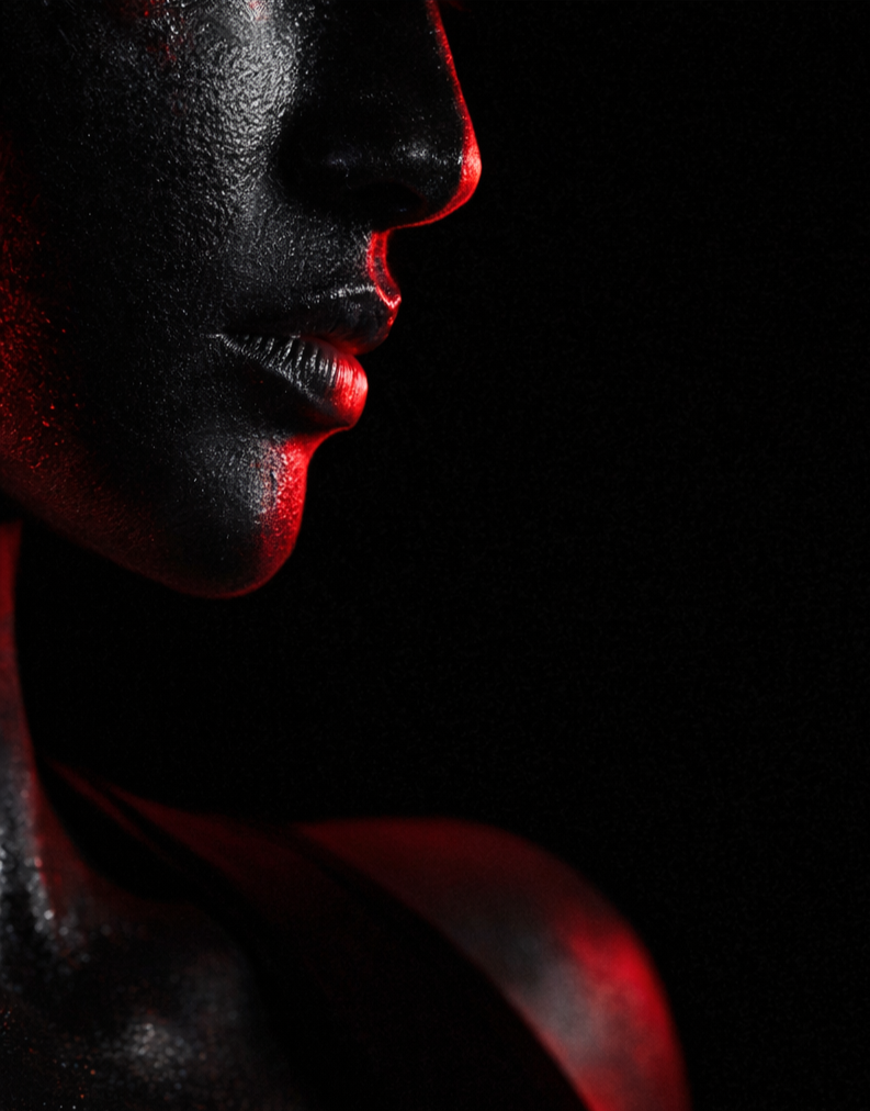 Close-up of a person's face and neck with wet skin, illuminated by red light against a black background.