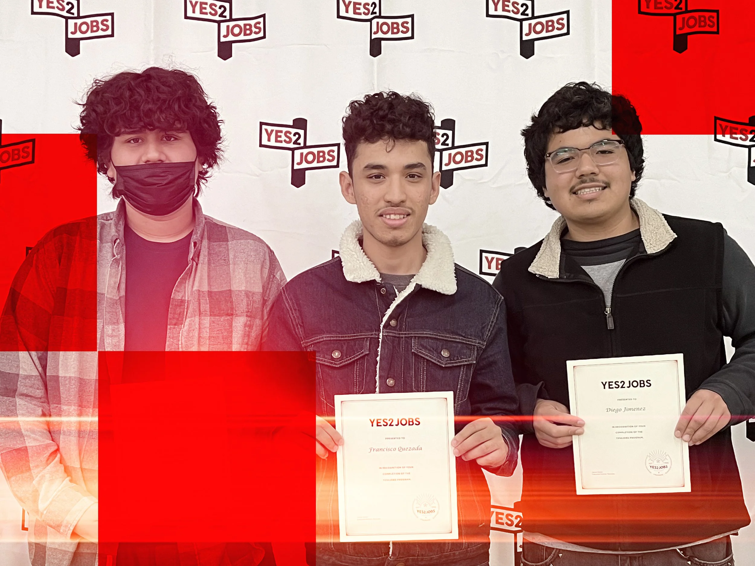 Three young men standing side by side holding certificates at a YES2 Jobs event. The background features a repeated YES2 JOBS logo. One man is wearing a face mask, the other two are smiling, and all are dressed in casual jackets.