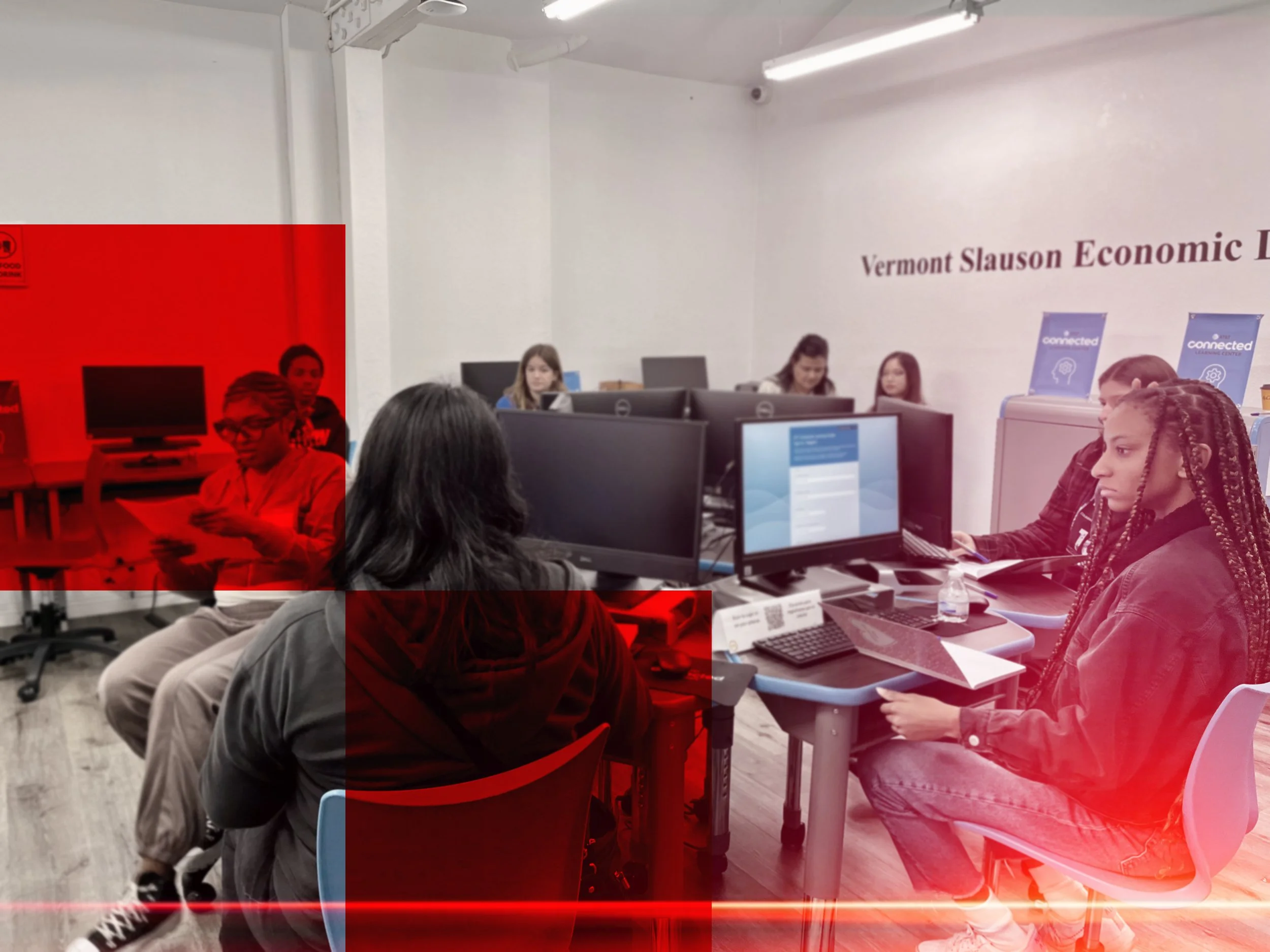Young people working on computers in a classroom or training center, with a sign reading 'Vermont Slauson Economic' on the wall.