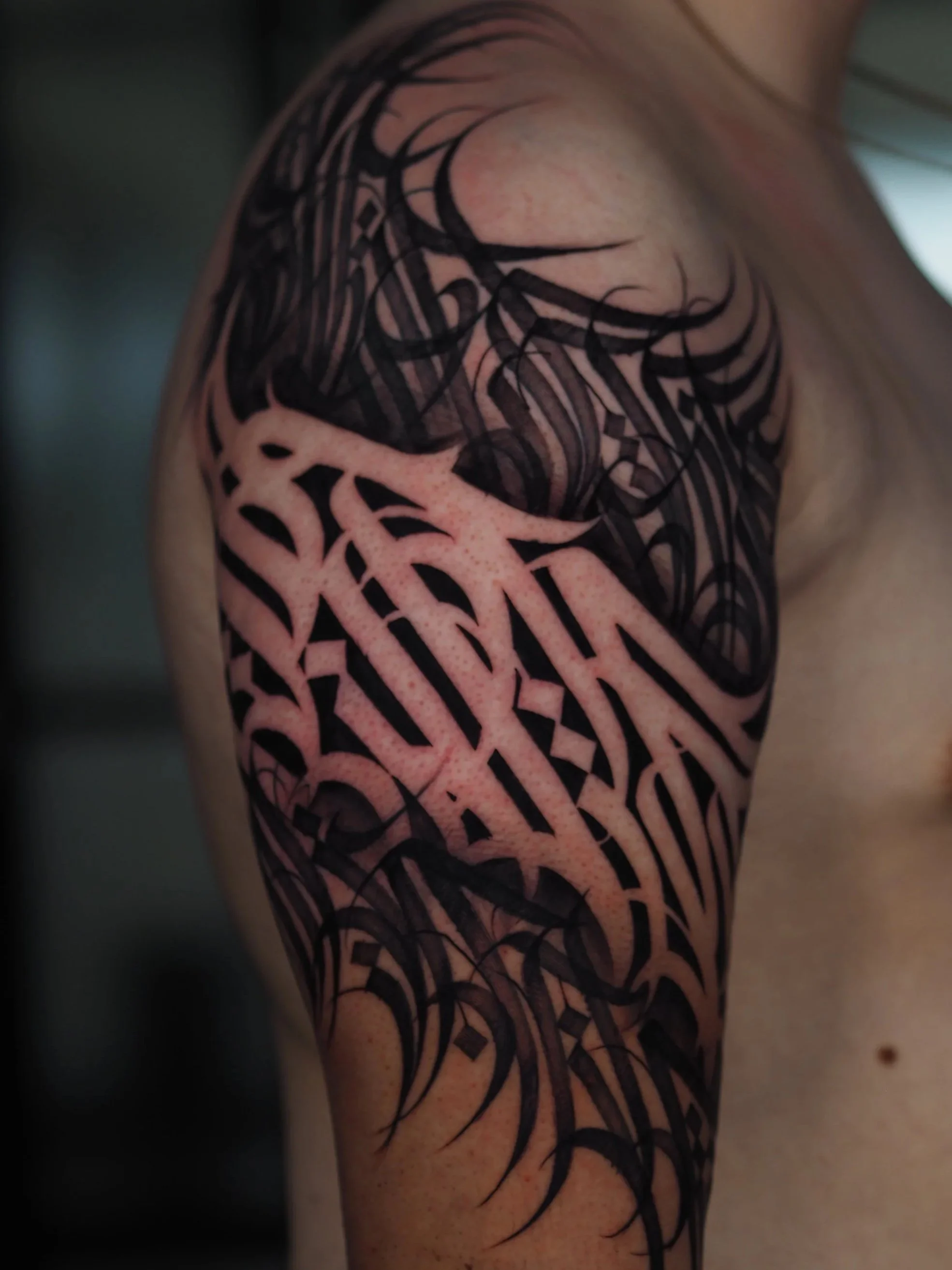 Close-up of a person’s shoulder with black tribal-style tattoo covering the upper arm and shoulder area.