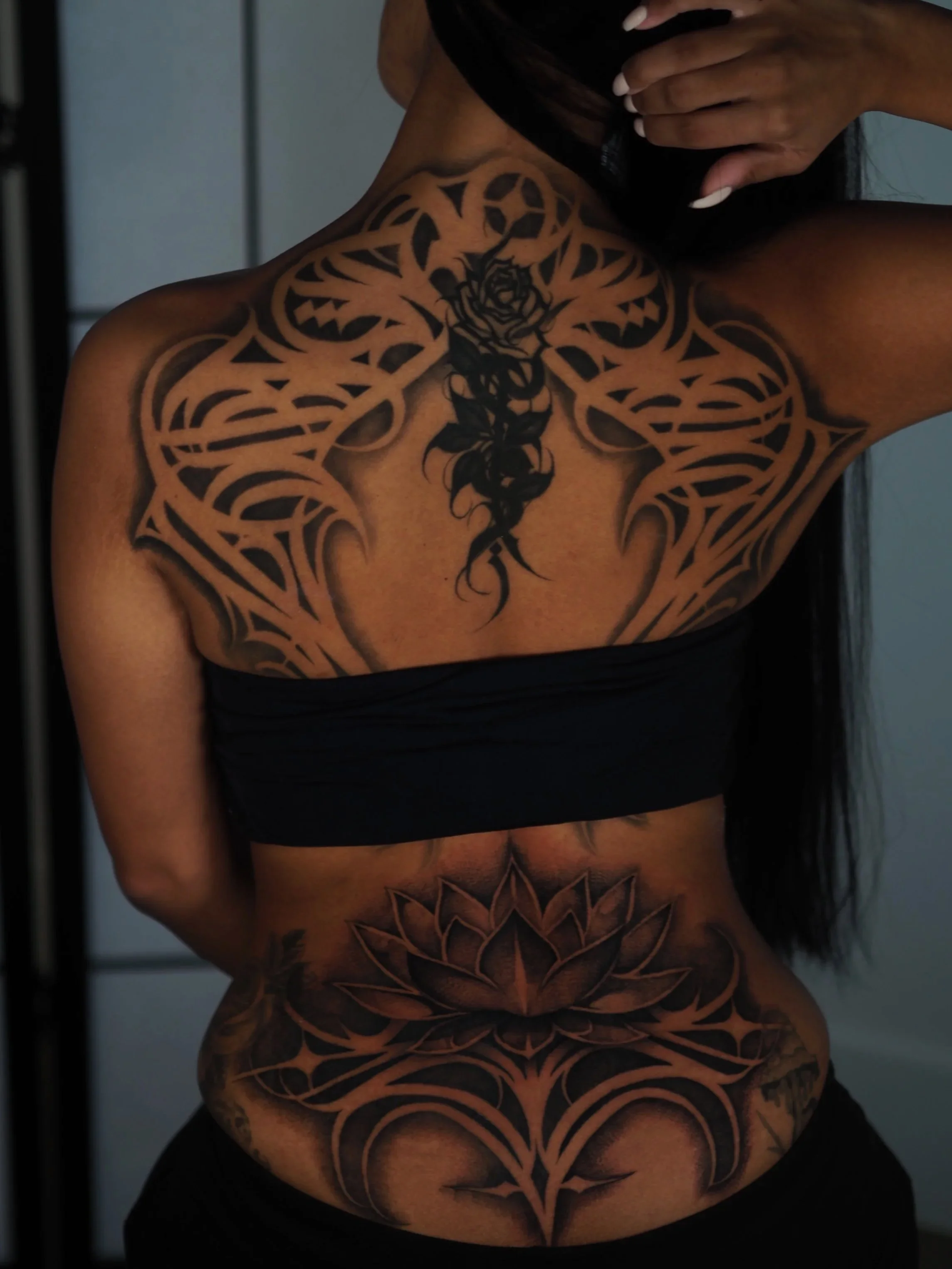 A person with a large tattoo covering their back, showing a floral and tribal design in black ink.