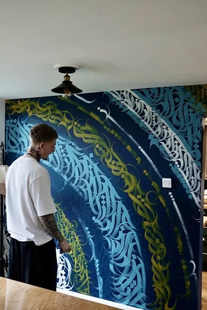 Person with tattoos on neck and arms looking at a large colorful mural with intricate abstract blue, green, and white patterns on a wall.