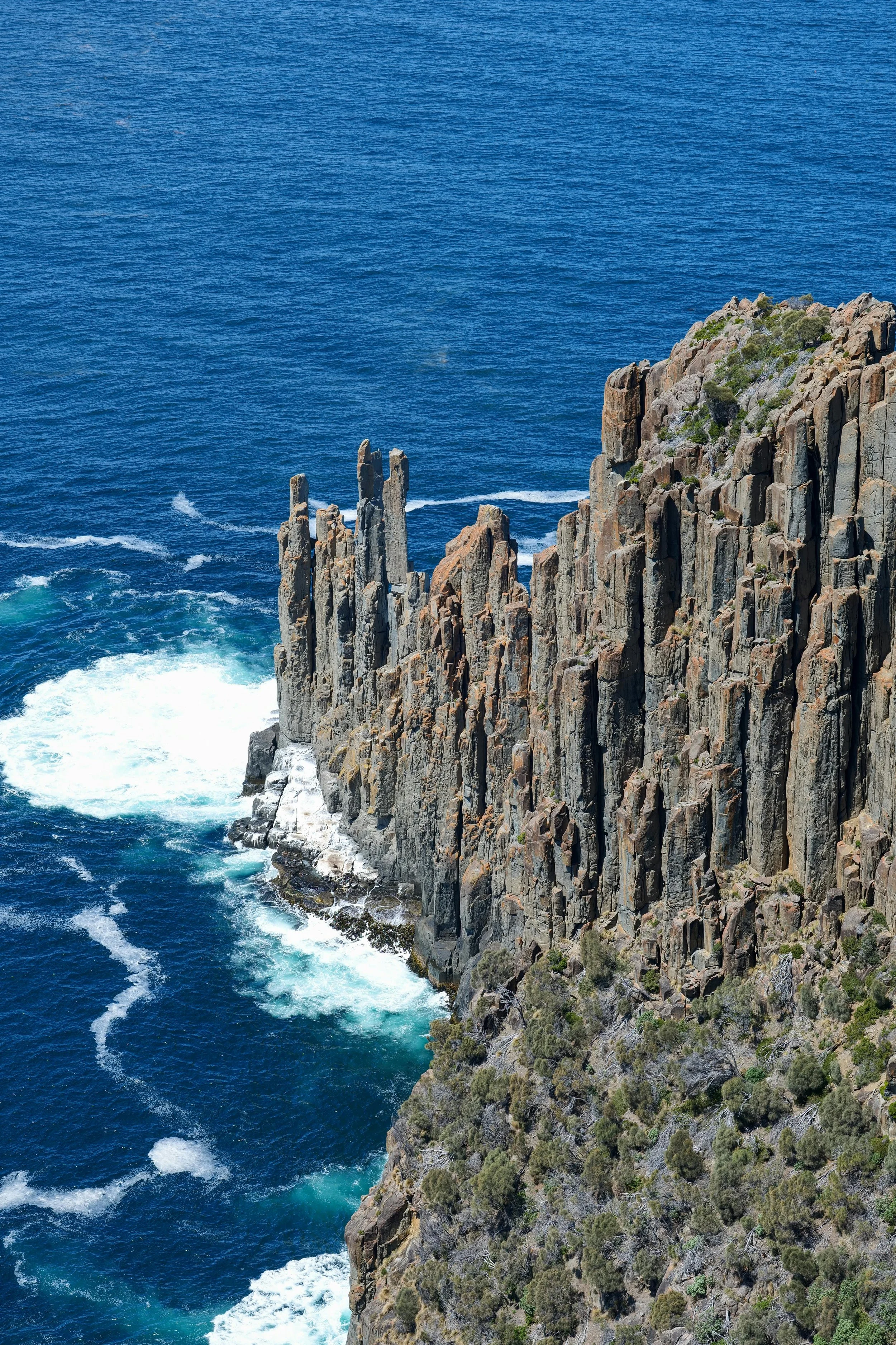 Rocky coastline with cliffs and sparse vegetation, overlooking the deep blue ocean with waves crashing against the rocks.