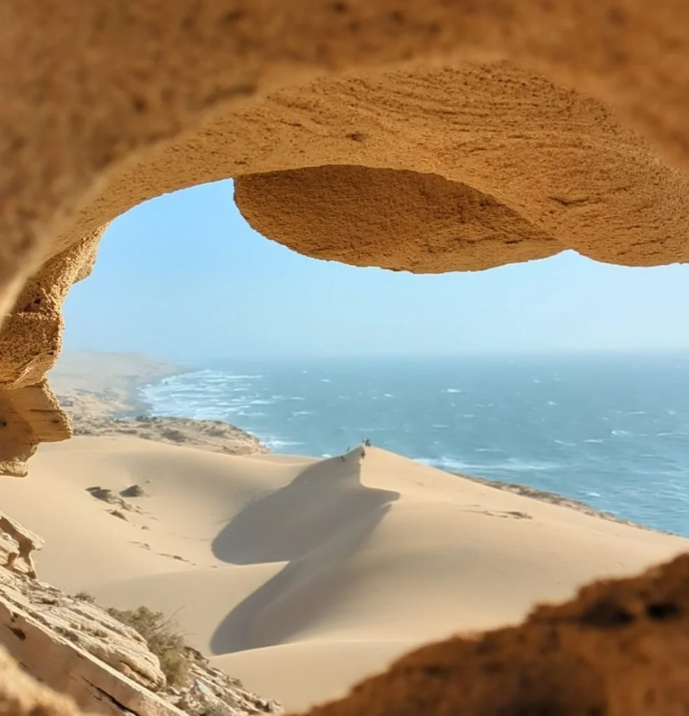 Vue d'une plage de dunes de sable vue à travers une ouverture dans une formation rocheuse