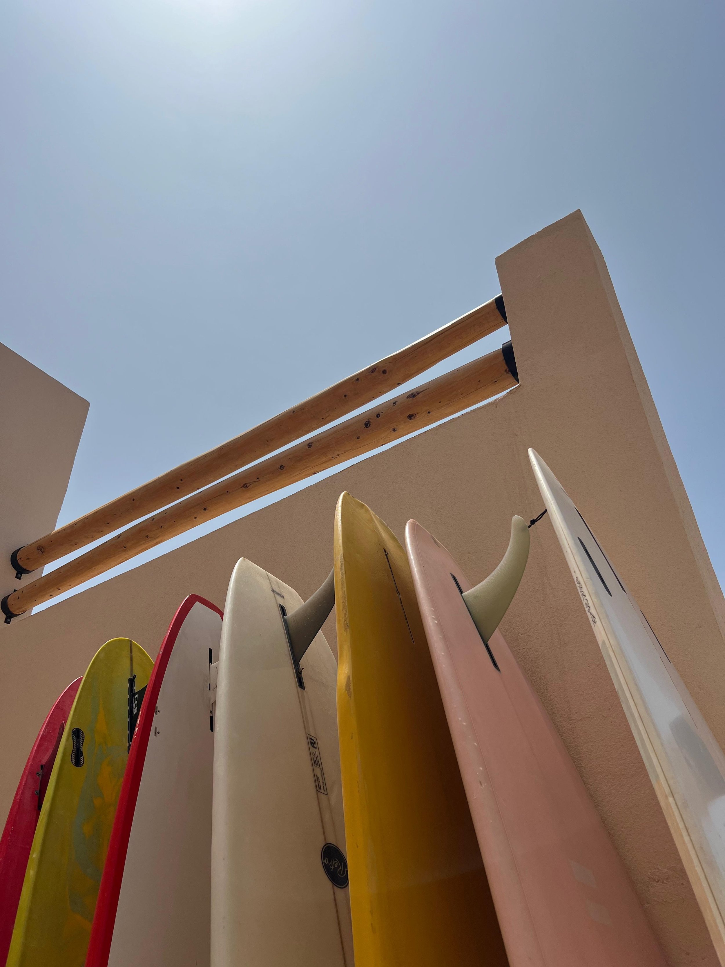 Planche de surf colorée suspendue avec tubes en bois au-dessus, vue de dessous contre le ciel bleu clair.