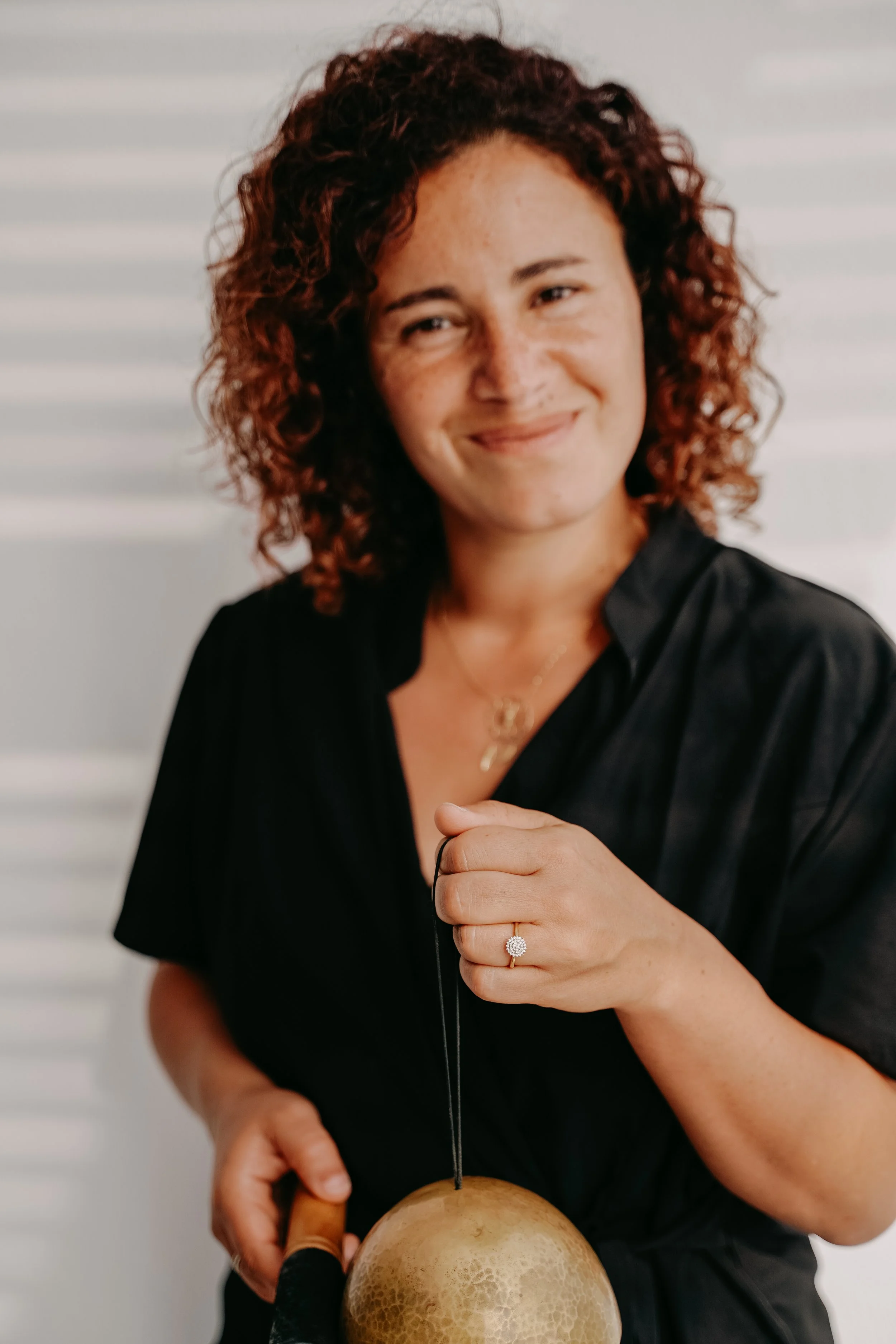 Femme souriante se préparant à faire pousser un champignon, tenant un tournevis, portant une bague en diamant et un collier, vêtue d'une chemise noire, debout devant un fond blanc avec des rayures