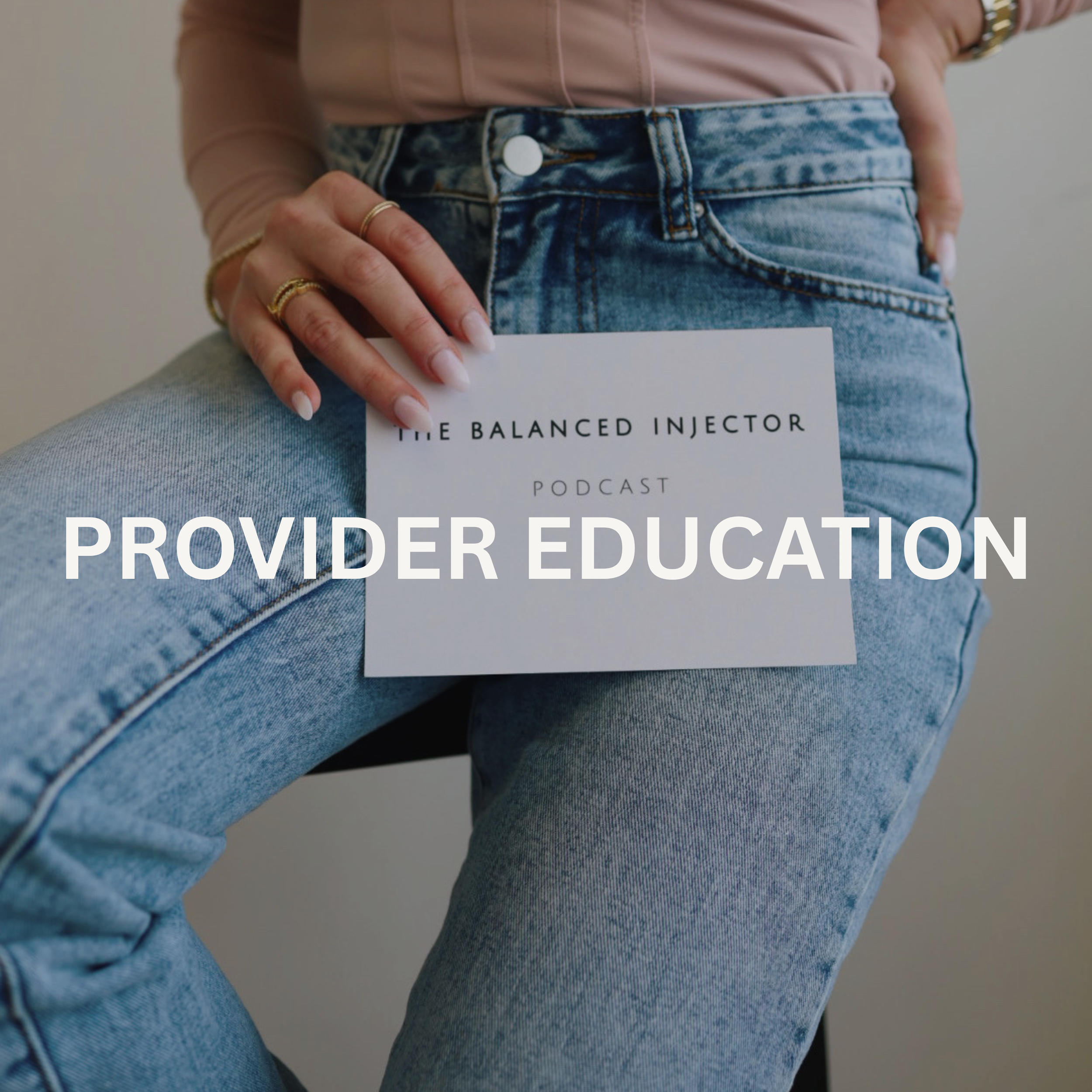 Close-up of a person wearing high-waisted, light blue, acid-wash jeans with a white button, paired with a beige or light pink long-sleeve shirt. The person is holding a white card or paper that partially covers their lap, with the visible text reading 'THE BALANCED INJECTOR PODCAST'. The person has multiple rings on their fingers and is wearing a watch on their wrist.