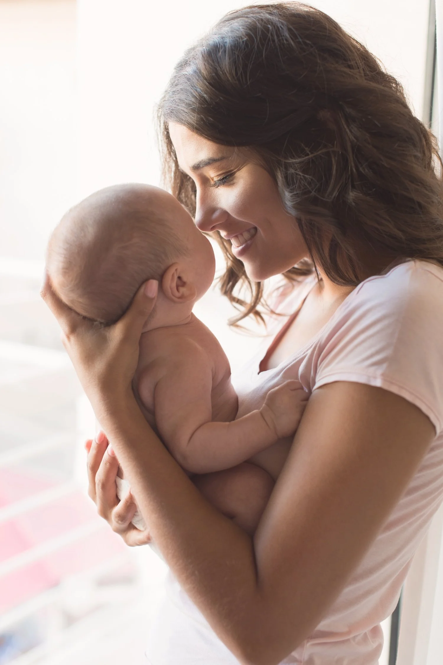 A woman with curly hair holding a smiling baby close to her face, both enjoying a tender moment at Tiny Feeding Co. in El Paso, TX where we provide lactation services, occupational therapy, therapeutic ultrasound, and mentorship for professionals.