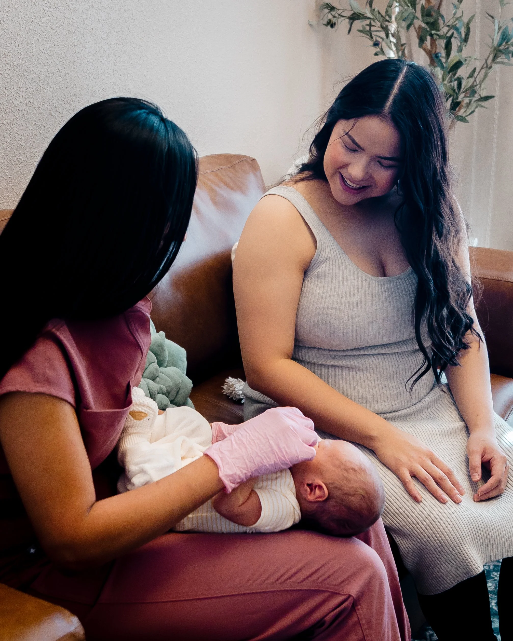 Jacklynn Knotts, OTR/L, IBCLC  is holding a newborn baby lying on her lap to work with her as her mom sits next to her while she shows her exercises and movements.
