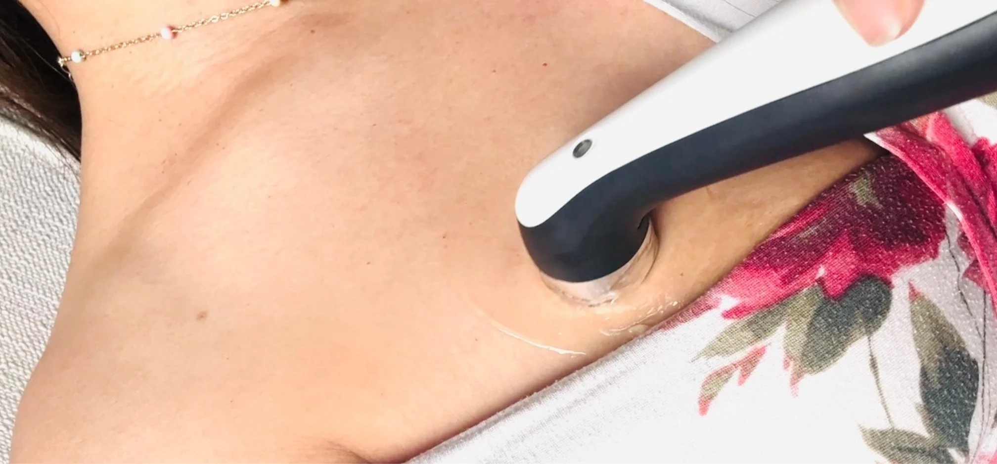 Close-up of a woman's breast tissue with an ultrasound wand on their chest, wearing a necklace and red patterned clothing at Tiny Feeding Co. where they provide therapeutic ultrasound to mothers in El Paso, TX for mastitis, clogged ducts, etc.