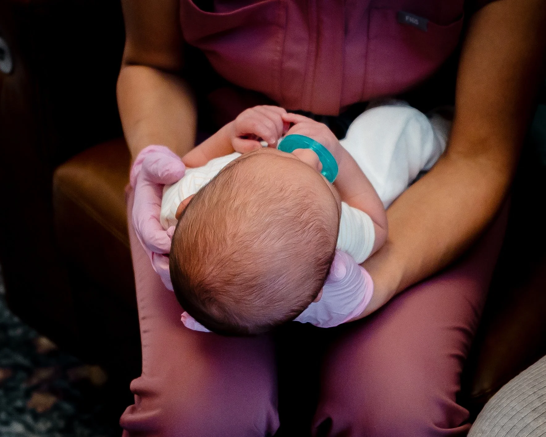 Baby being held in supine with 2 pinked gloves with a teal pacifier in their mouth you can see the head of dark, fine hair. This is a photo for Tiny Feeding Co. in El Paso, Texas focusing on lactation services, OT, and therapeutic ultrasound