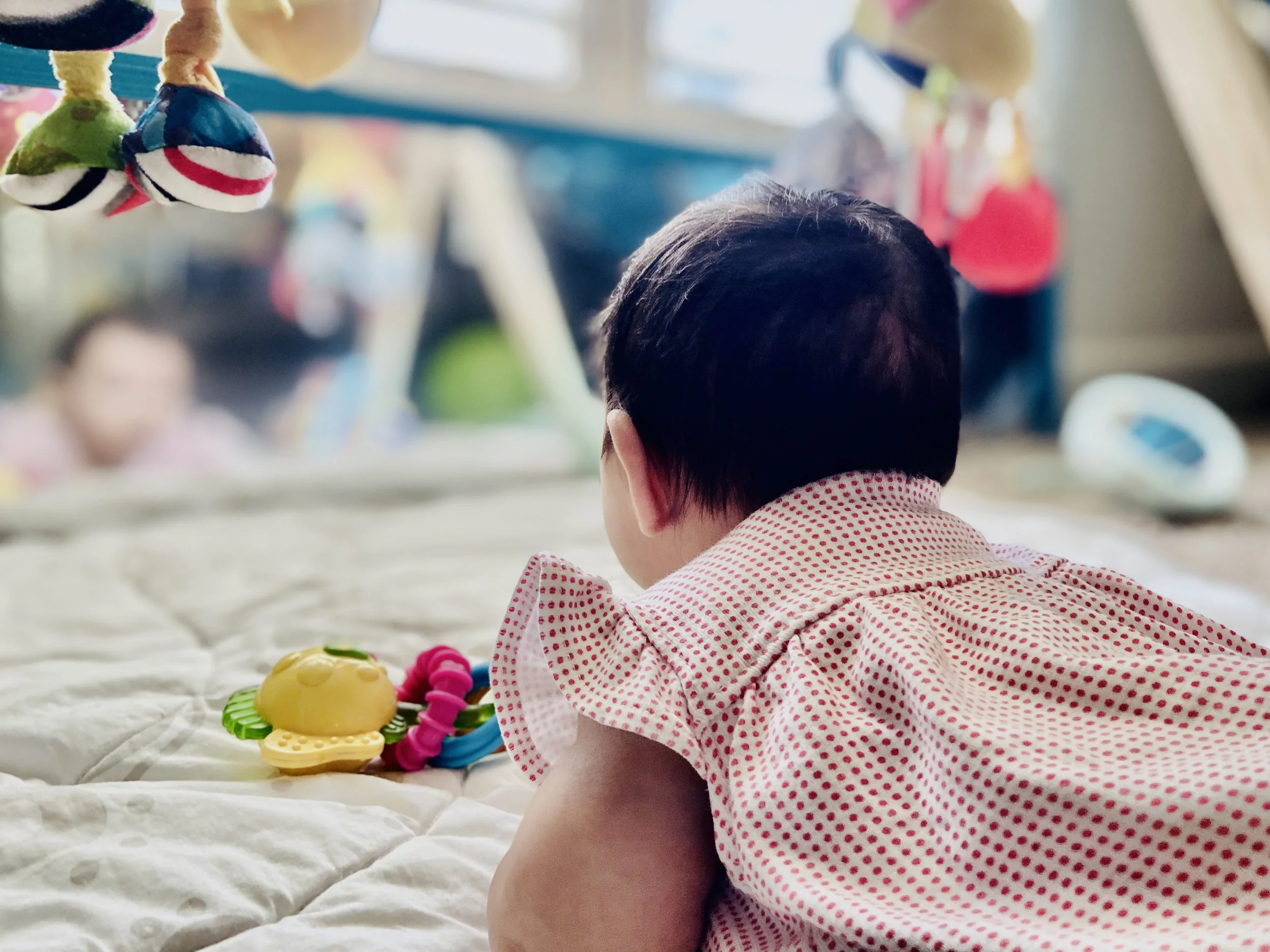 Baby sitting on a blanket with colorful toys and plush objects hanging above during an occupational therapy sessions at Tiny Feeding Co. in El Paso, TX