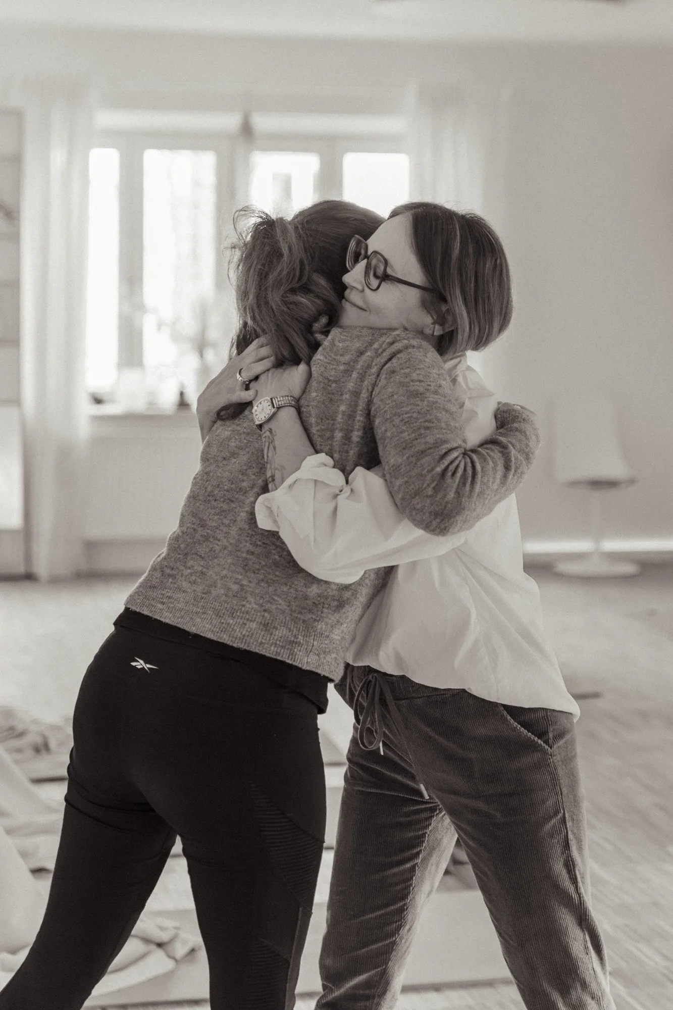 Zwei Frauen umarmen sich herzlich in einem hellen Raum, der vermutlich ein Wohnzimmer ist.