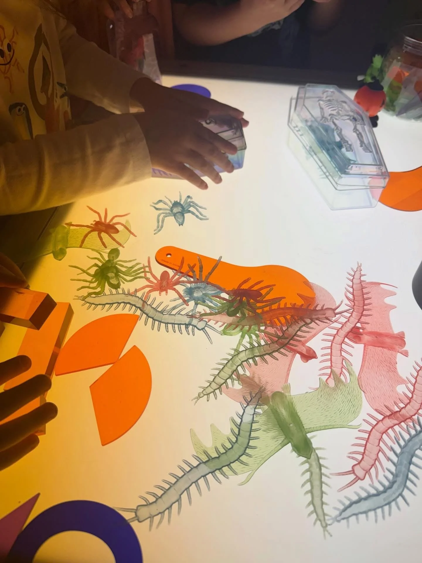 Children engaging in a hands-on educational activity involving colorful paper cutouts of various insects and creatures, with a LEGO brick on the table.
