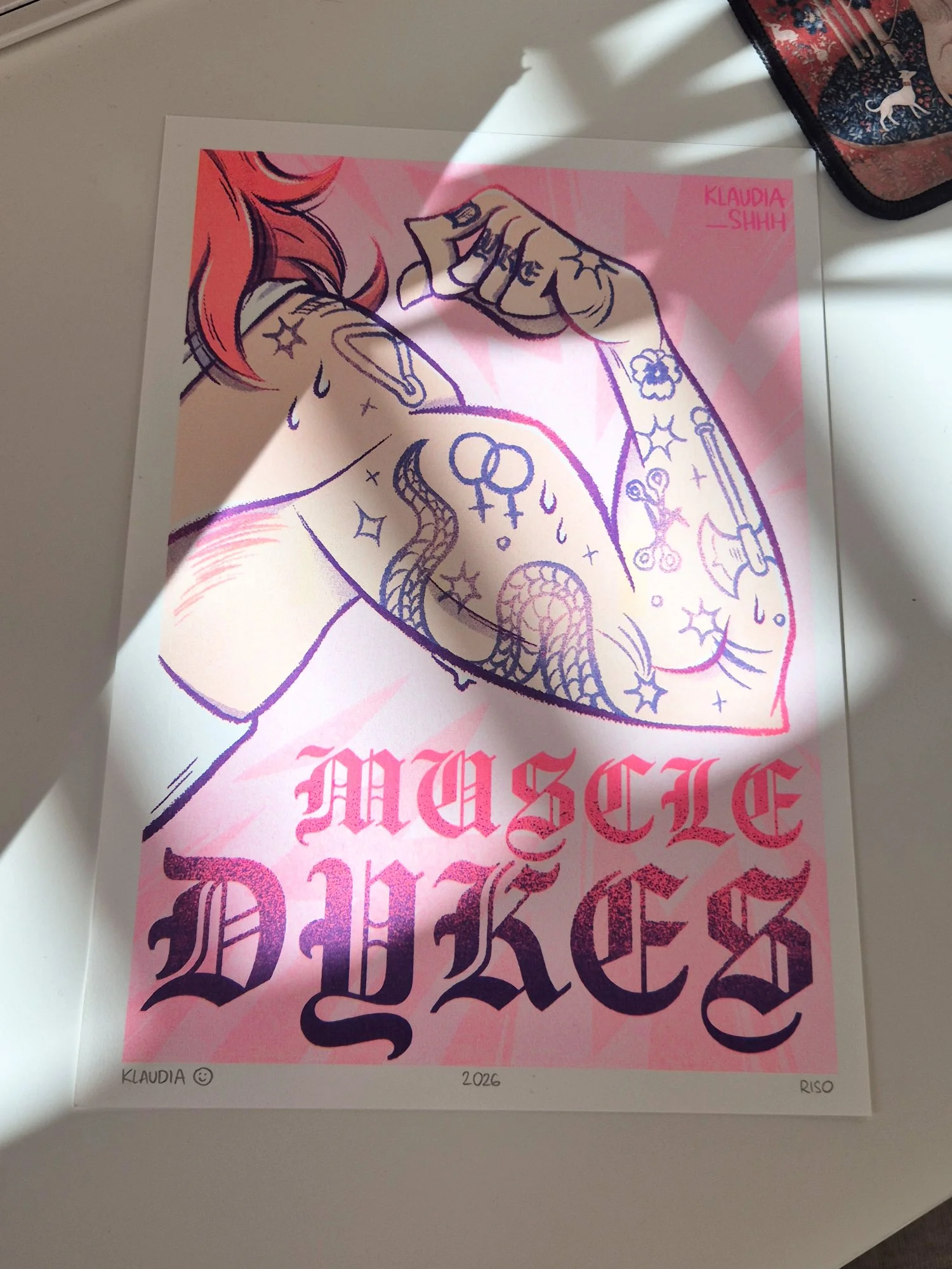 Photo of the same print laying on a desk, with sun highlighting the fluo pink ink