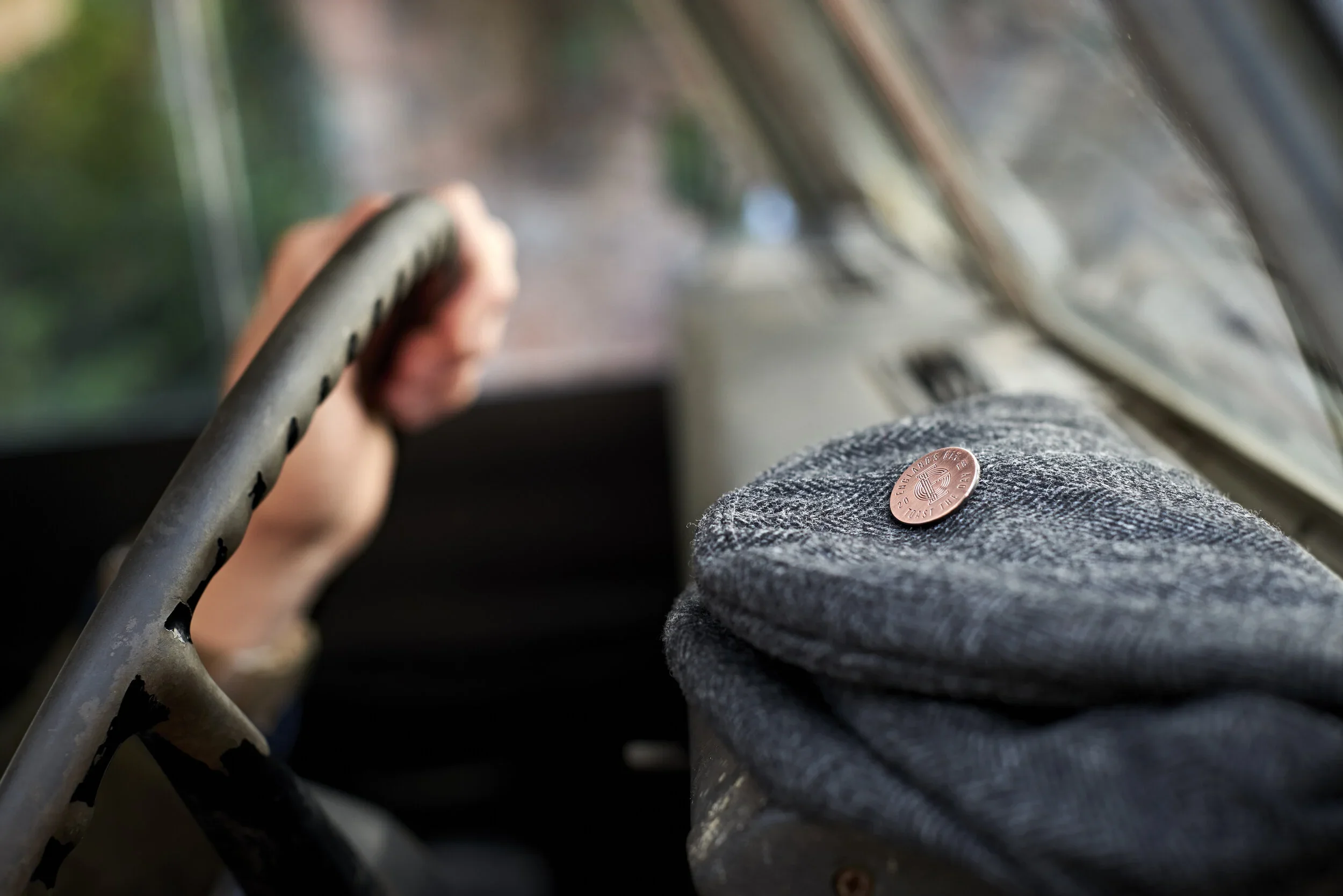 A person holds a gray handlebar inside a vehicle, with a gray socked foot resting on a surface featuring a copper penny. The background is blurred, showing trees and sunlight.