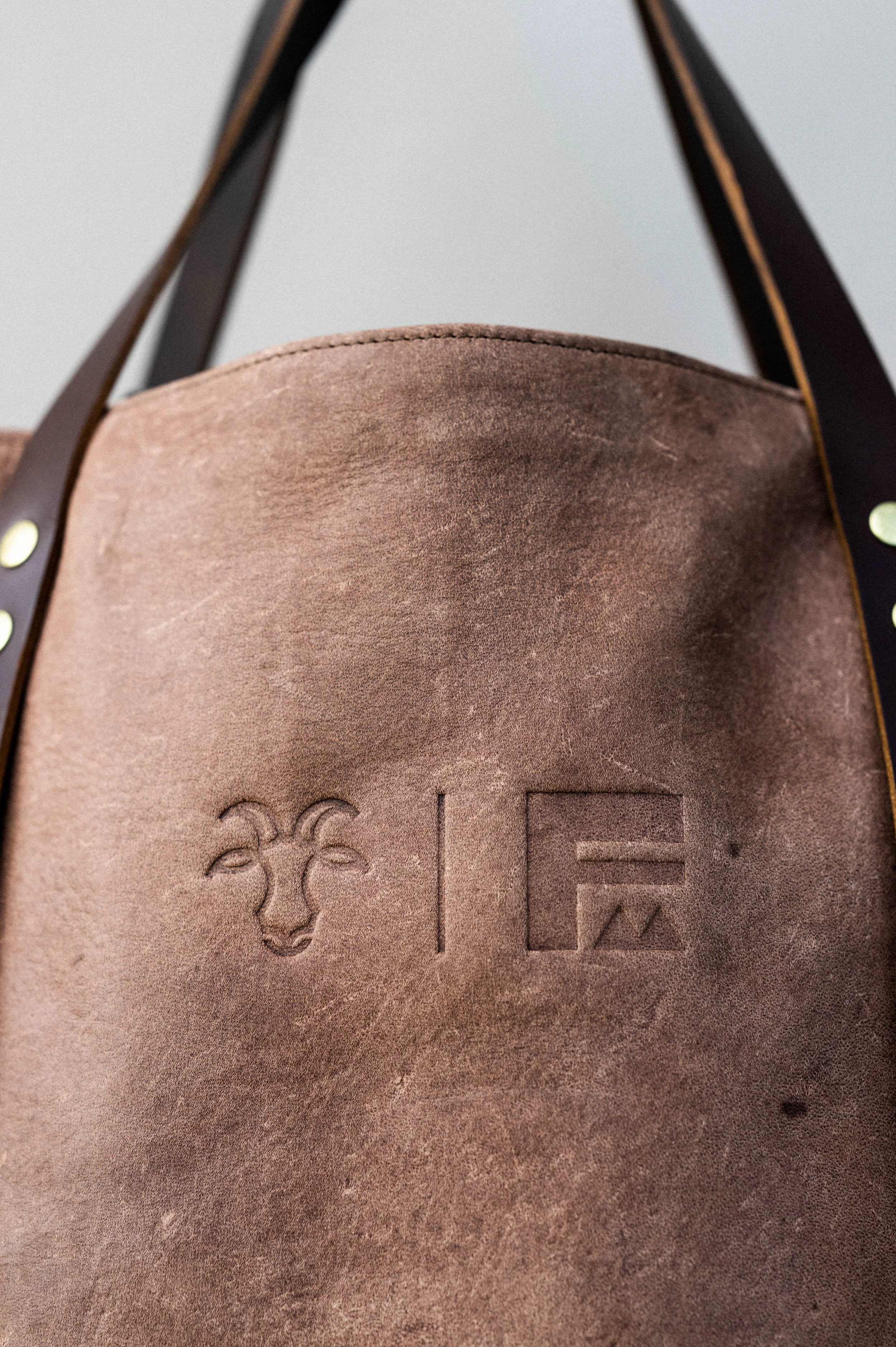 Close-up of a brown leather bag with embossed decorative skull and logo, with black straps and gold rivets.