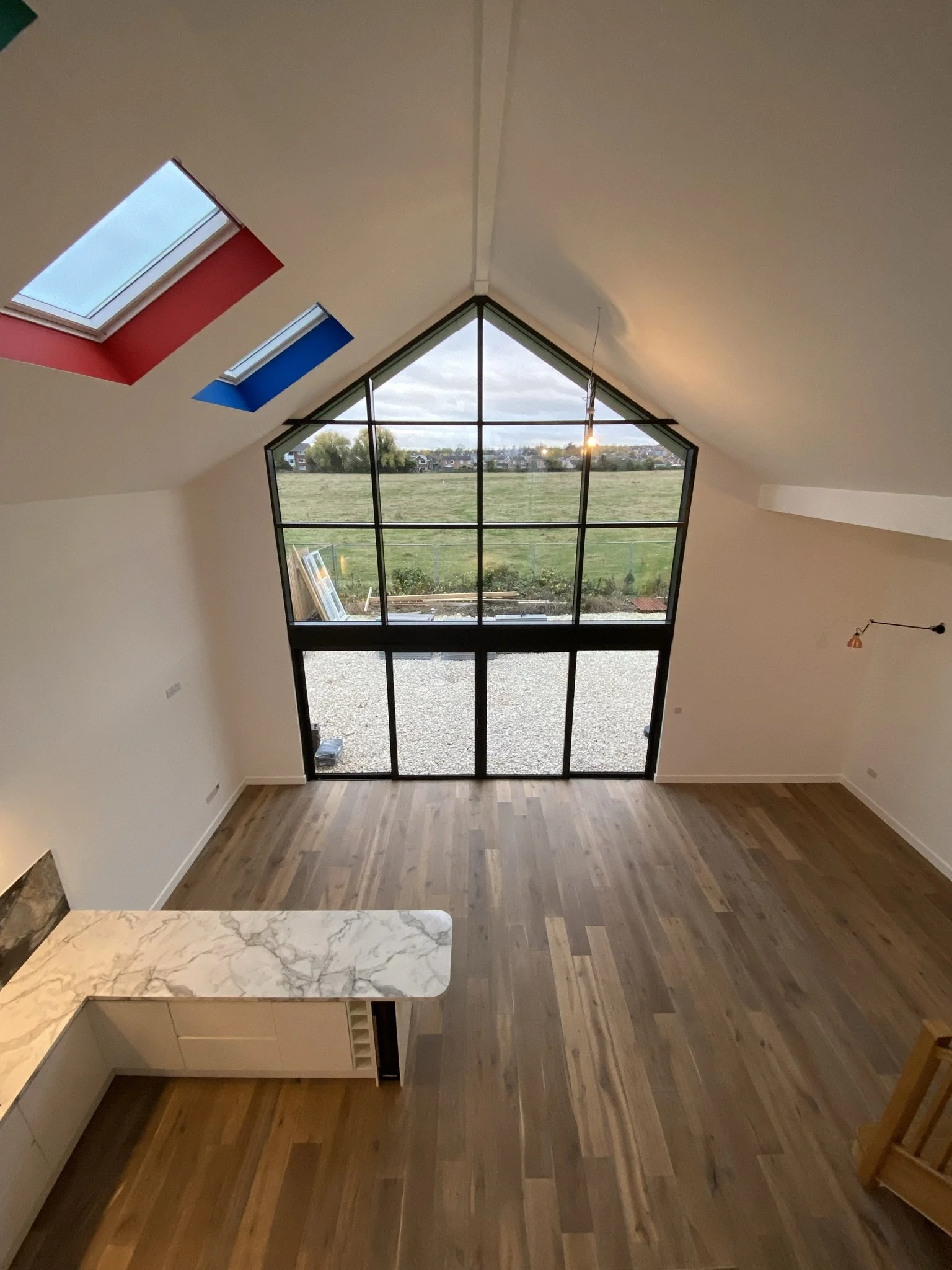 Interior view of a modern living space with large floor-to-ceiling windows, wooden flooring, and skylights in a vaulted ceiling.