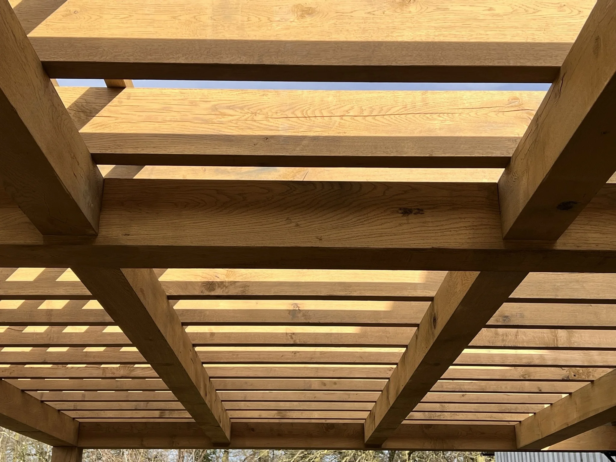 Looking up at a wooden pergola with horizontal slats, showing the sky through the gaps.