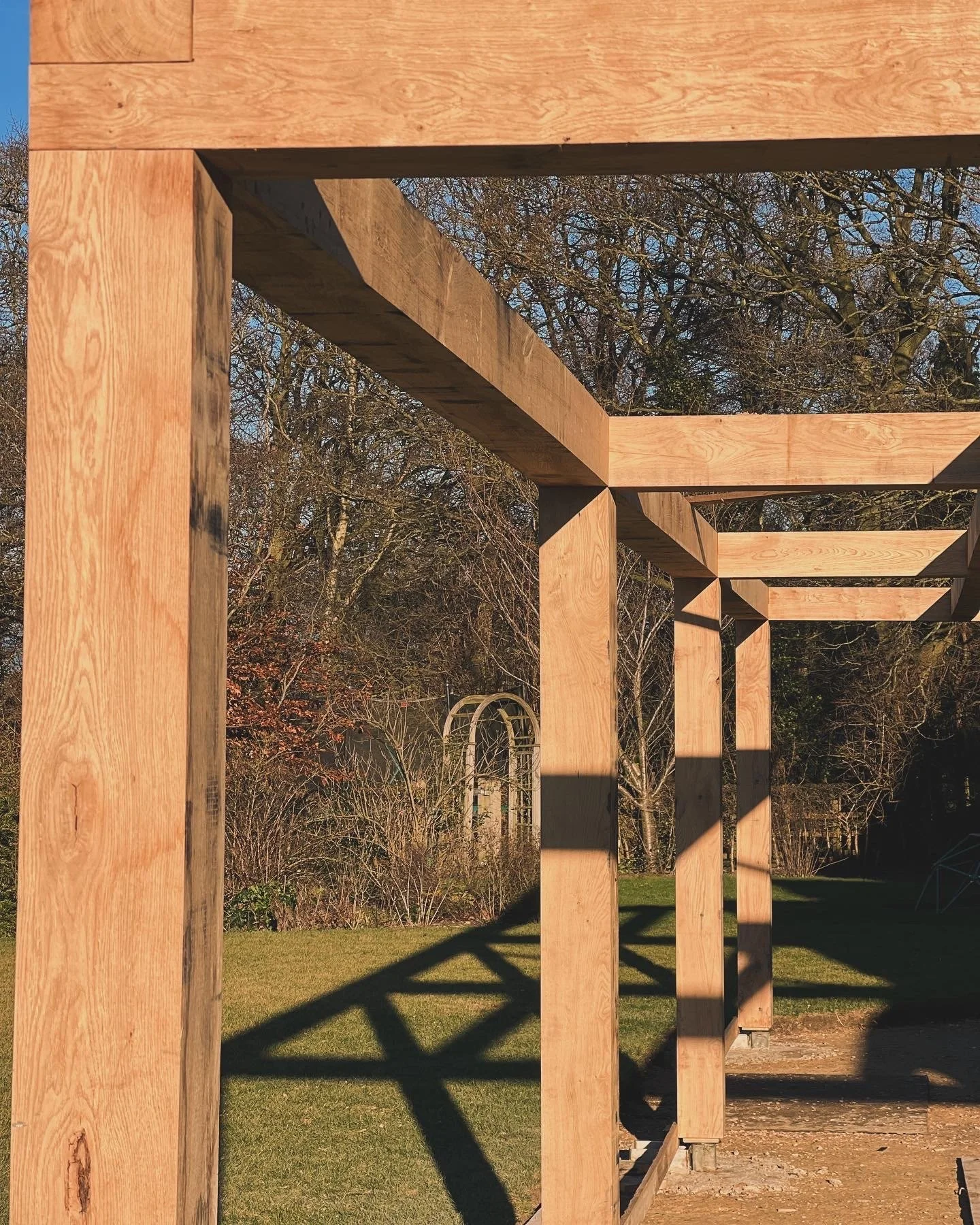 Wooden framework structure outdoors with trees and a grassy lawn in the background.