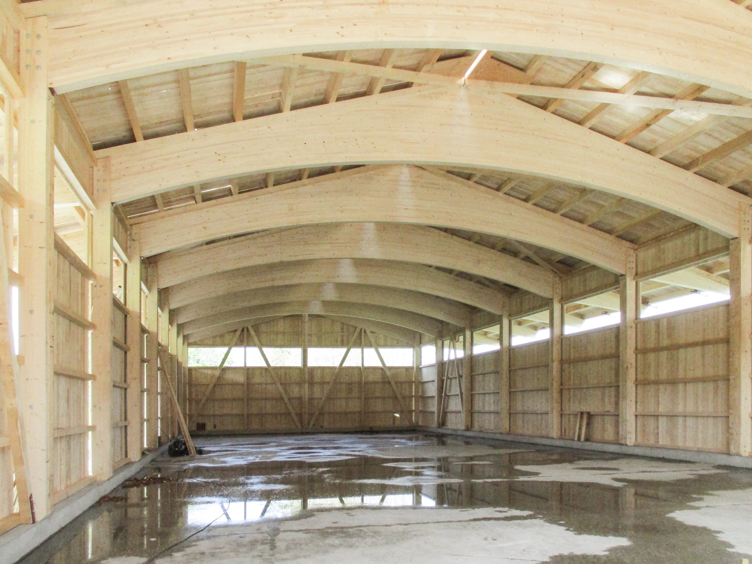 Innenraum eines Holzgebäudes im Bau, mit sichtbaren Holzbalken und Deckenkonstruktion, noch im Rohbauzustand.