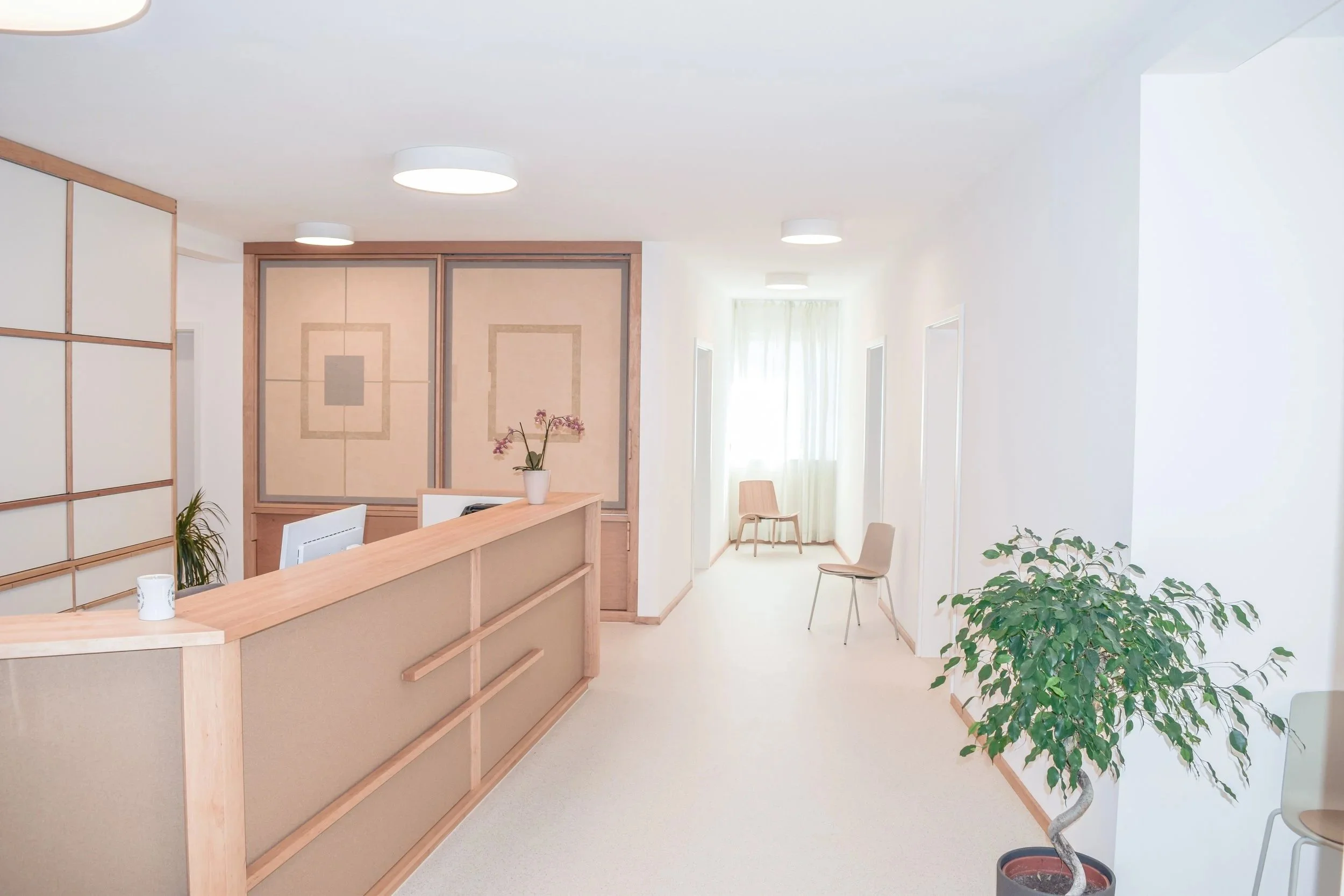 Heller, moderner Innenraum mit weißen Wänden, Holzmöbeln, Pflanzen und Sitzgelegenheiten.