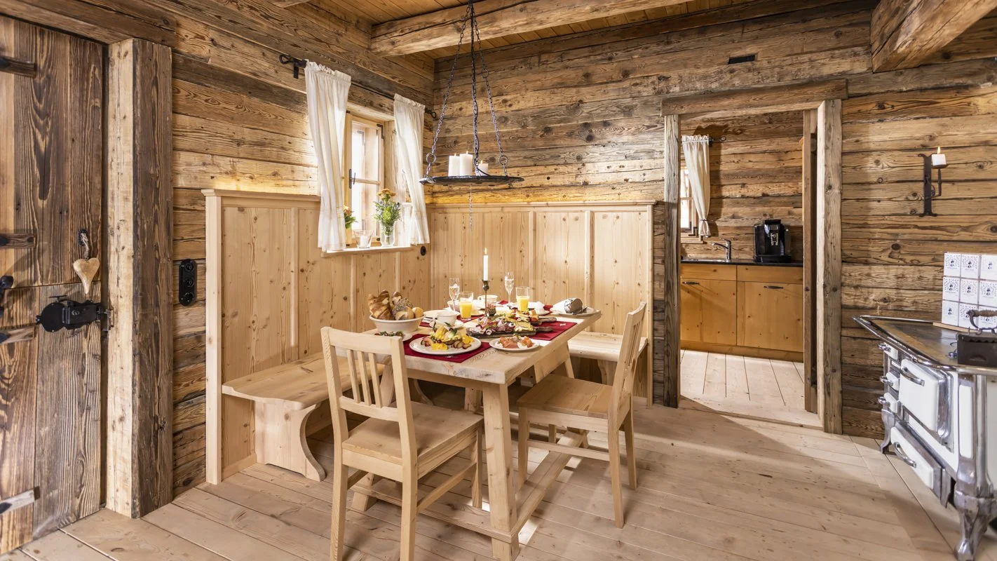 Gemütlicher rustikaler Holz-Küchenraum mit Esstisch und Fenstern, Tisch ist für Frühstück gedeckt.
