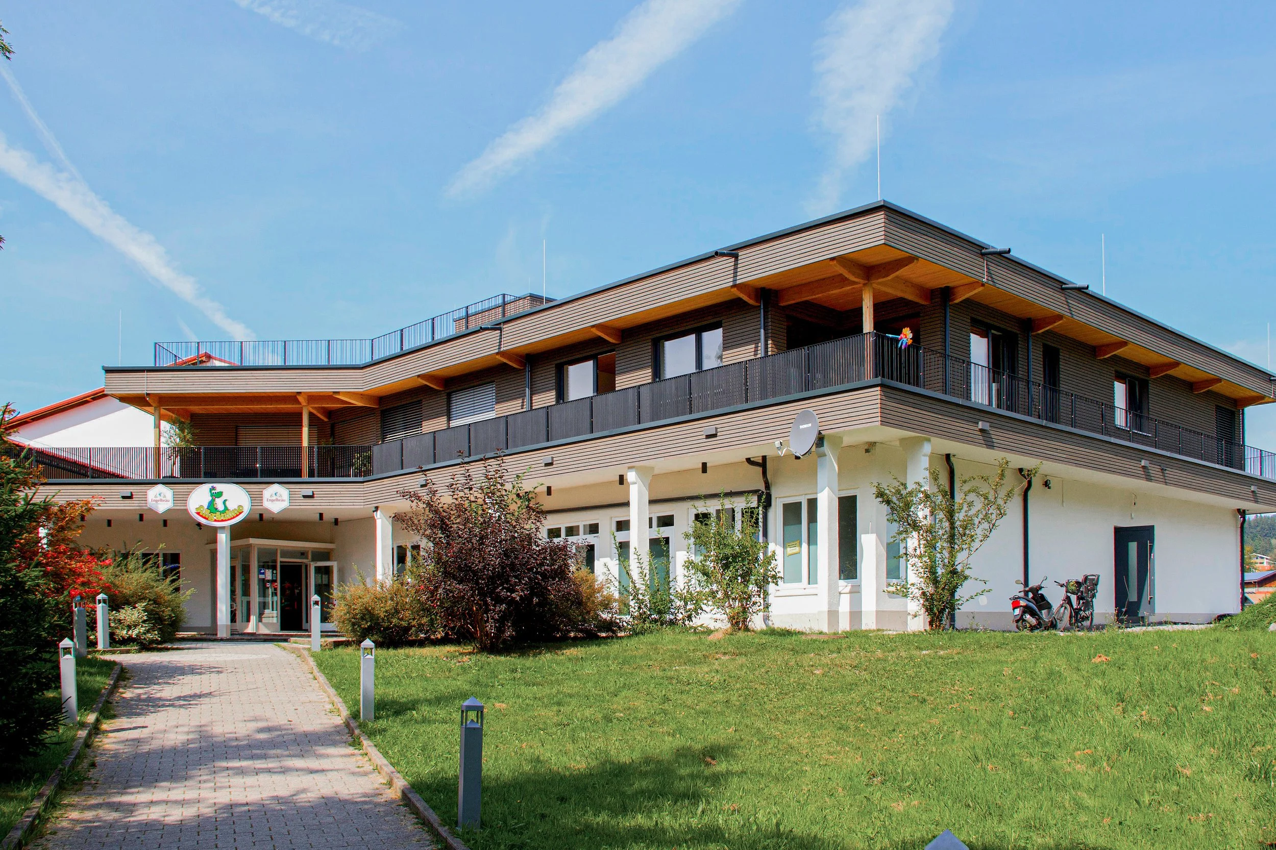 Mehrstöckiges modernes Gebäude mit Balkonflächen, Garten und Fahrrad im Vordergrund, blauer Himmel mit Wolken im Hintergrund.