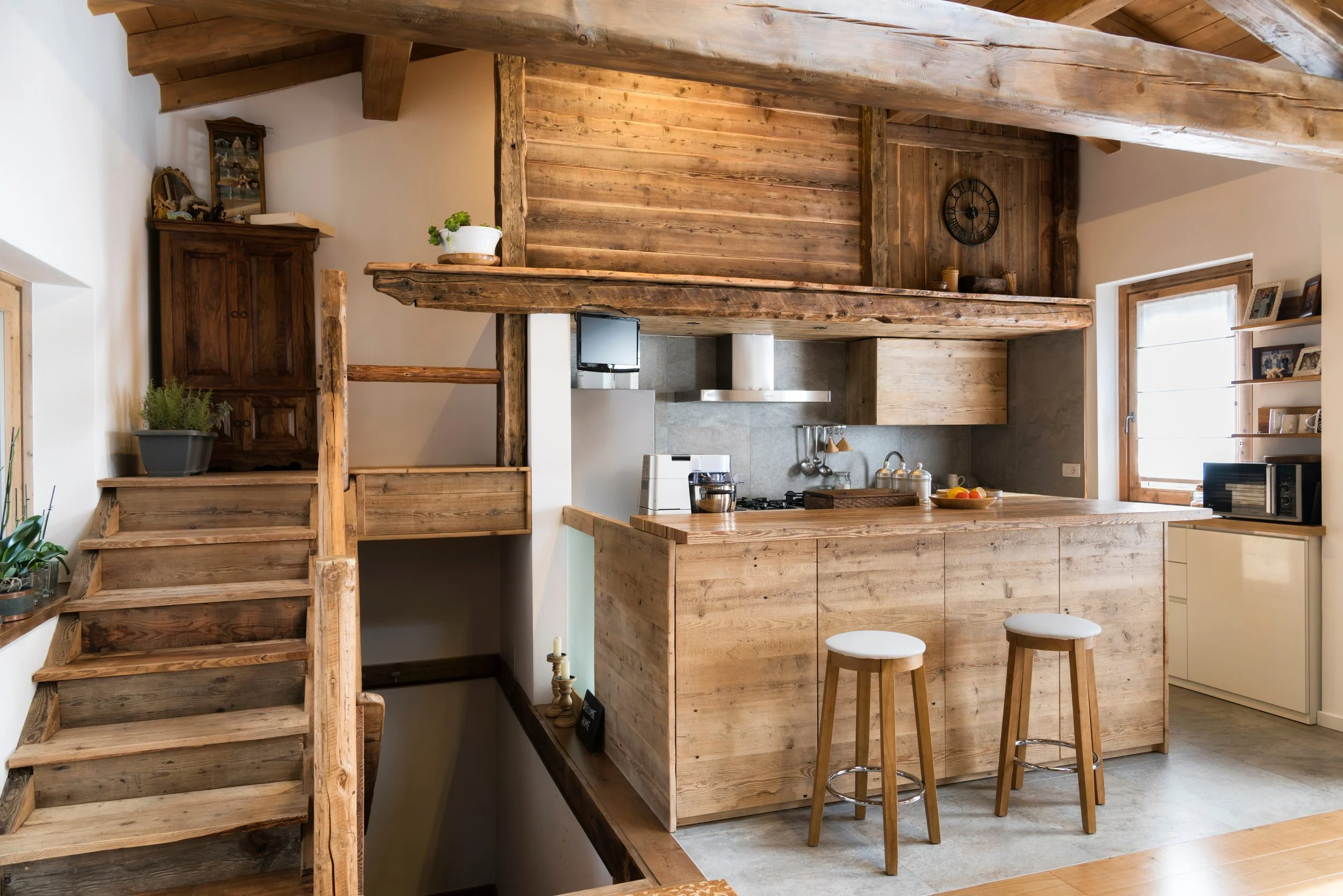 Ein Holz-Küchenbereich mit einer Holzbar, zwei Barhockern, einem Herd, einem Fenster und Holzregalen.