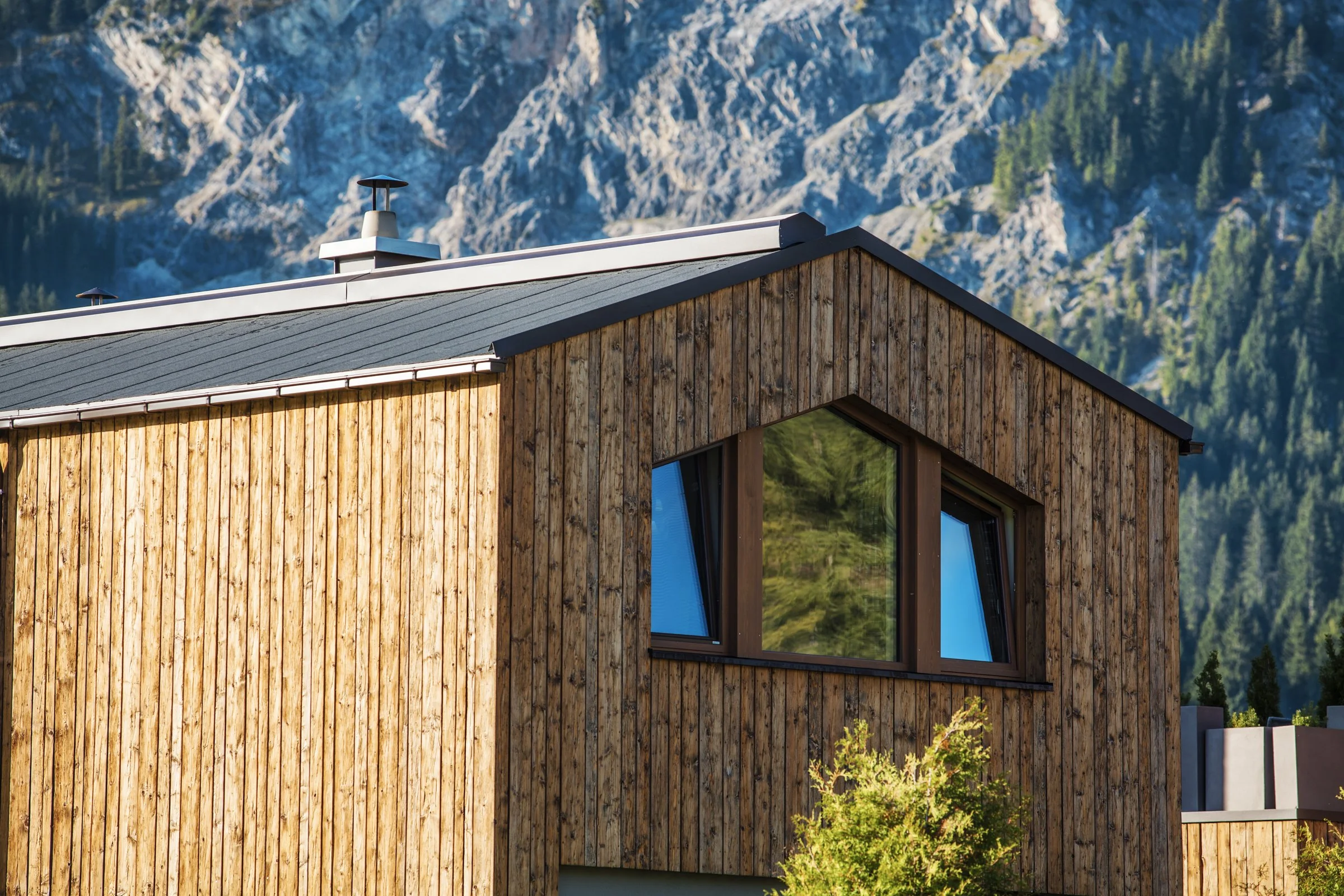Modernes Holzhaus mit großen Fenstern vor Bergkulisse.