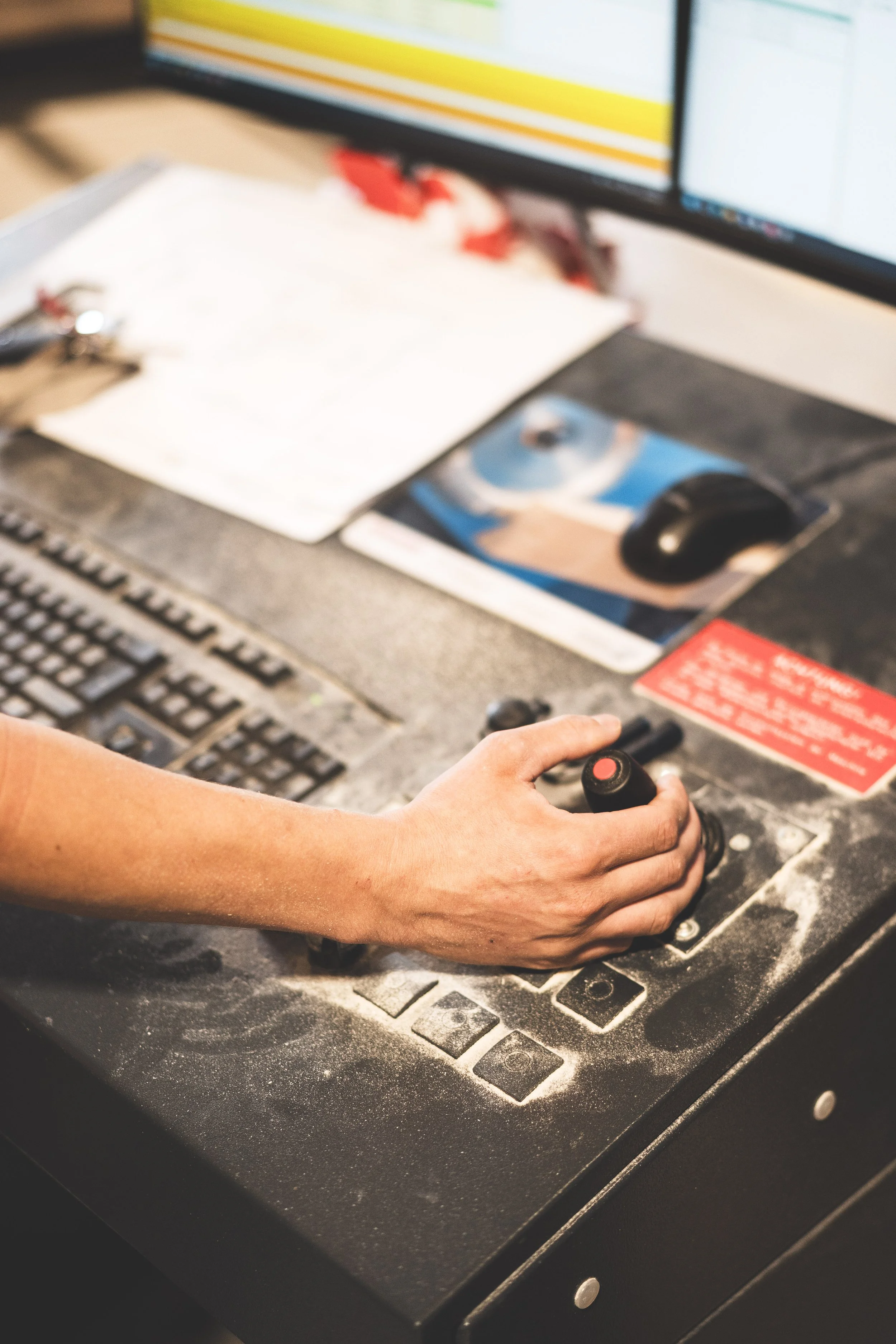 Eine Hand hält einen Joystick, der über einem Arbeitstisch mit einer Tastatur und einem Computerbildschirm, auf dem Diagramme zu sehen sind.