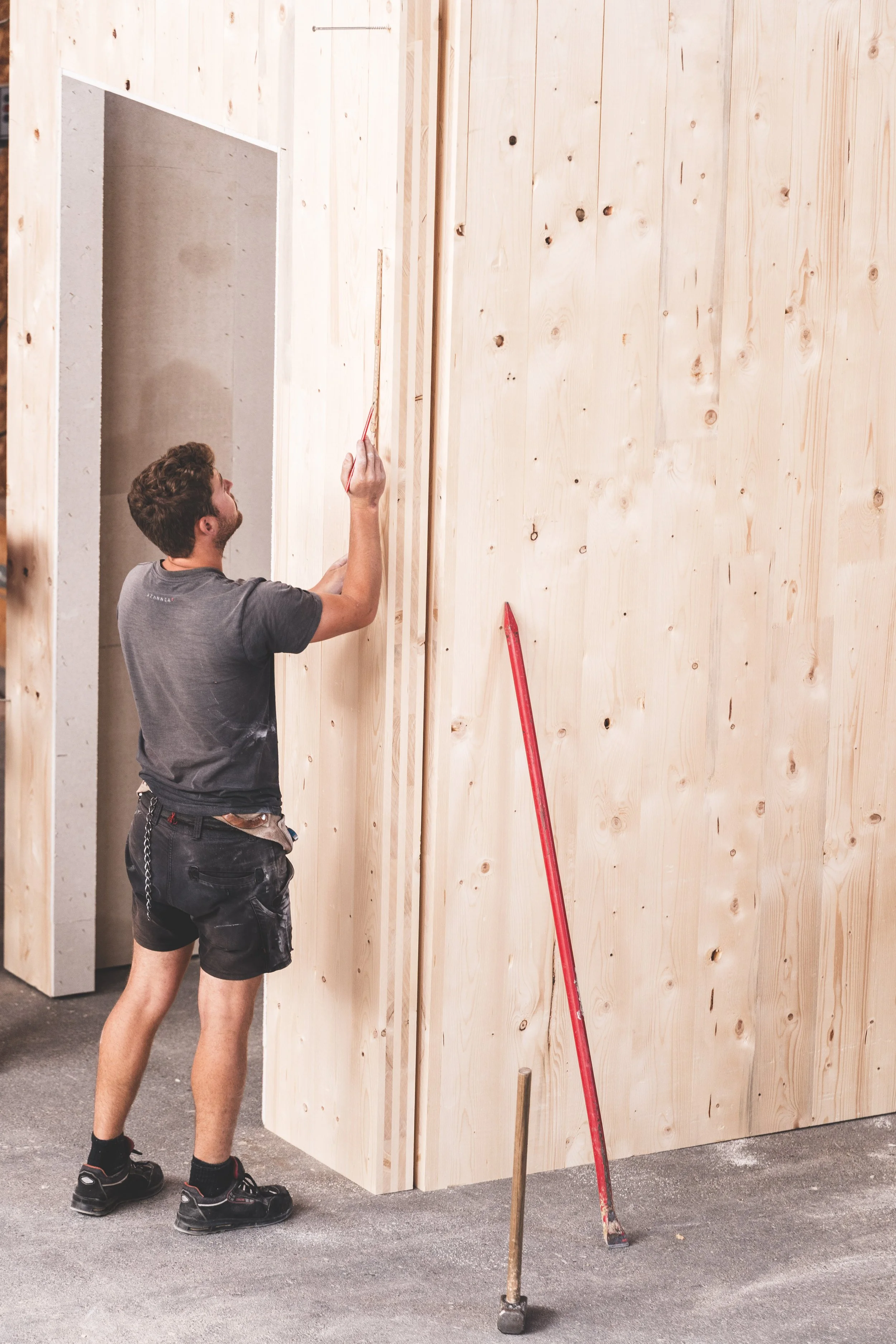 Mann bei der Arbeit mit Holzrahmen in einem Raum unter Verwendung eines Zollstocks, in einer Baustelle oder Werkstatt.