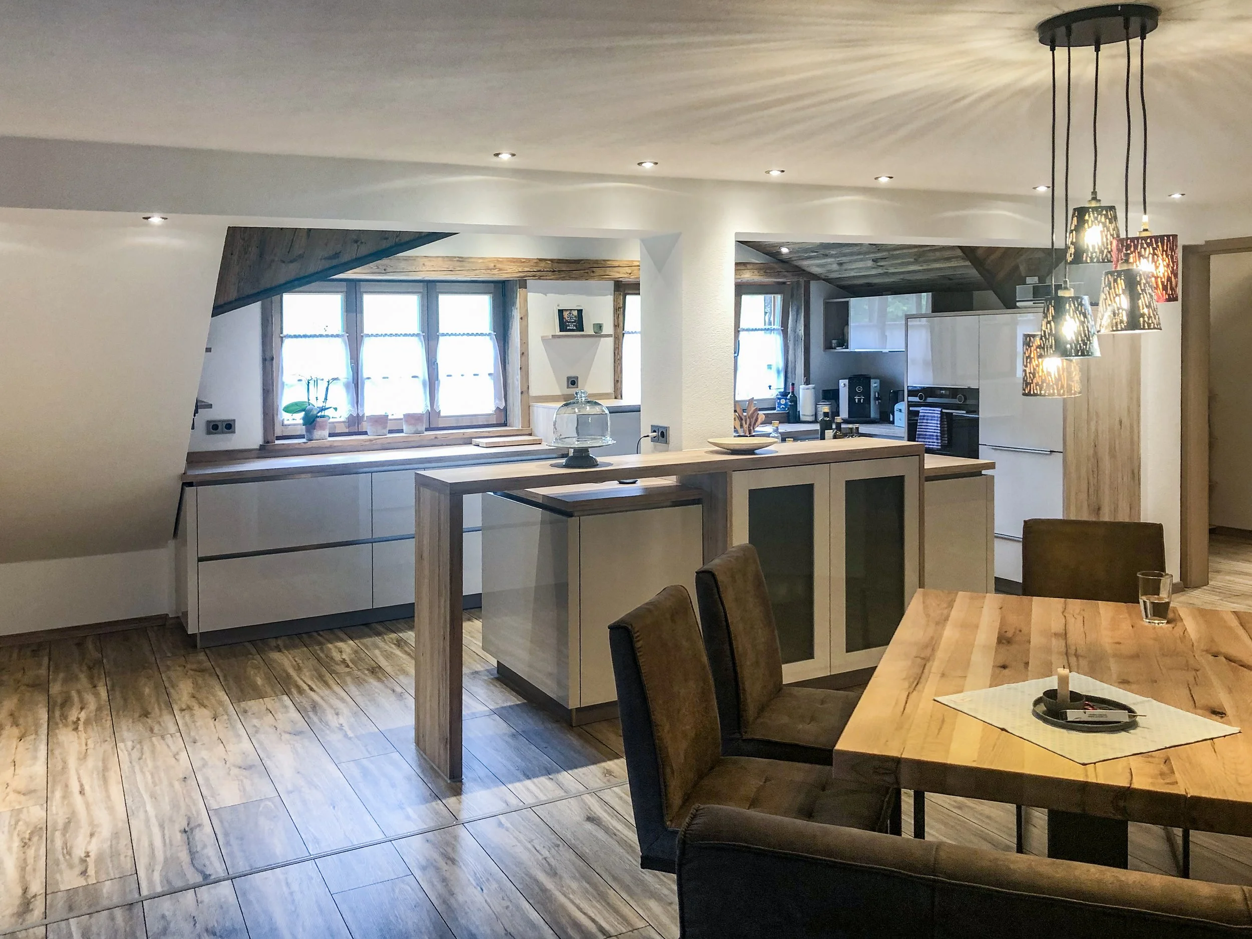 Innenansicht einer modernen Küchen- und Essbereich mit Holzleisten, großen Fenstern, hängenden Lampen und Holzfußboden.