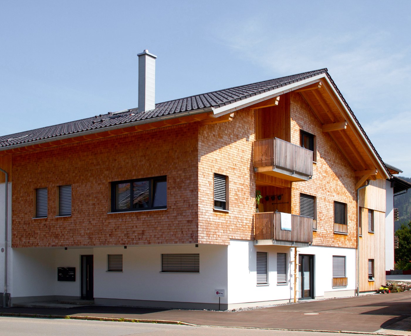 Modernes Mehrfamilienhaus mit Ziegelwandfassade und Holzbalconies, unter einem schrägen Dach, bei sonnigem Wetter.