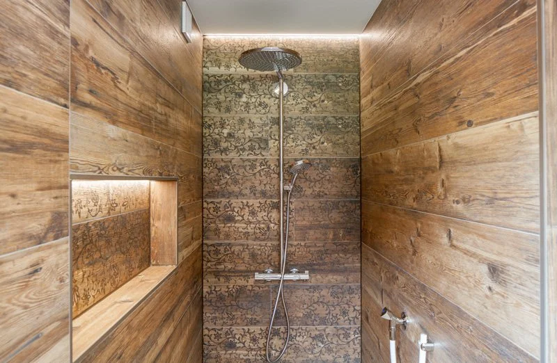 Moderner Duschraum mit Holzverkleidung und einer Wand mit dekorativem Muster, Duschkopf an der Decke und Thermostatarmatur an der Wand.