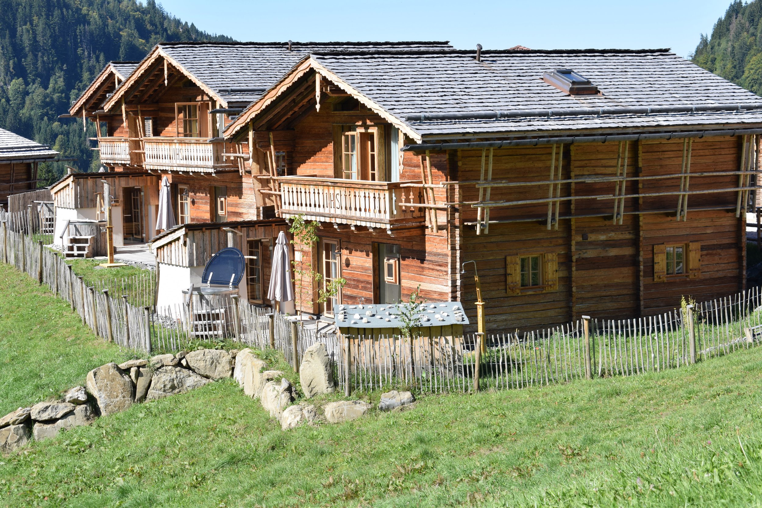 Holzhäuser mit Balconies in einer bergigen, grünen Landschaft bei sonnigem Wetter.