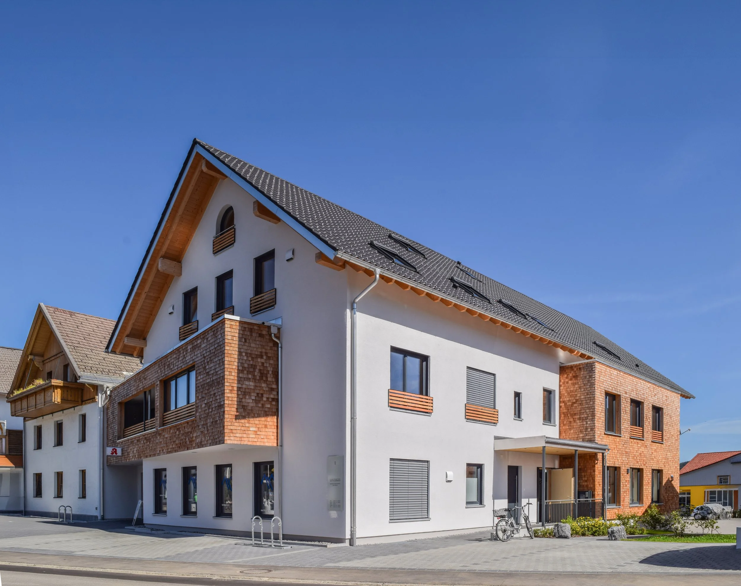 Modernes Mehrfamilienhaus mit weißen Wänden, brick-Elementen und einem schrägen Dach unter blauem Himmel.