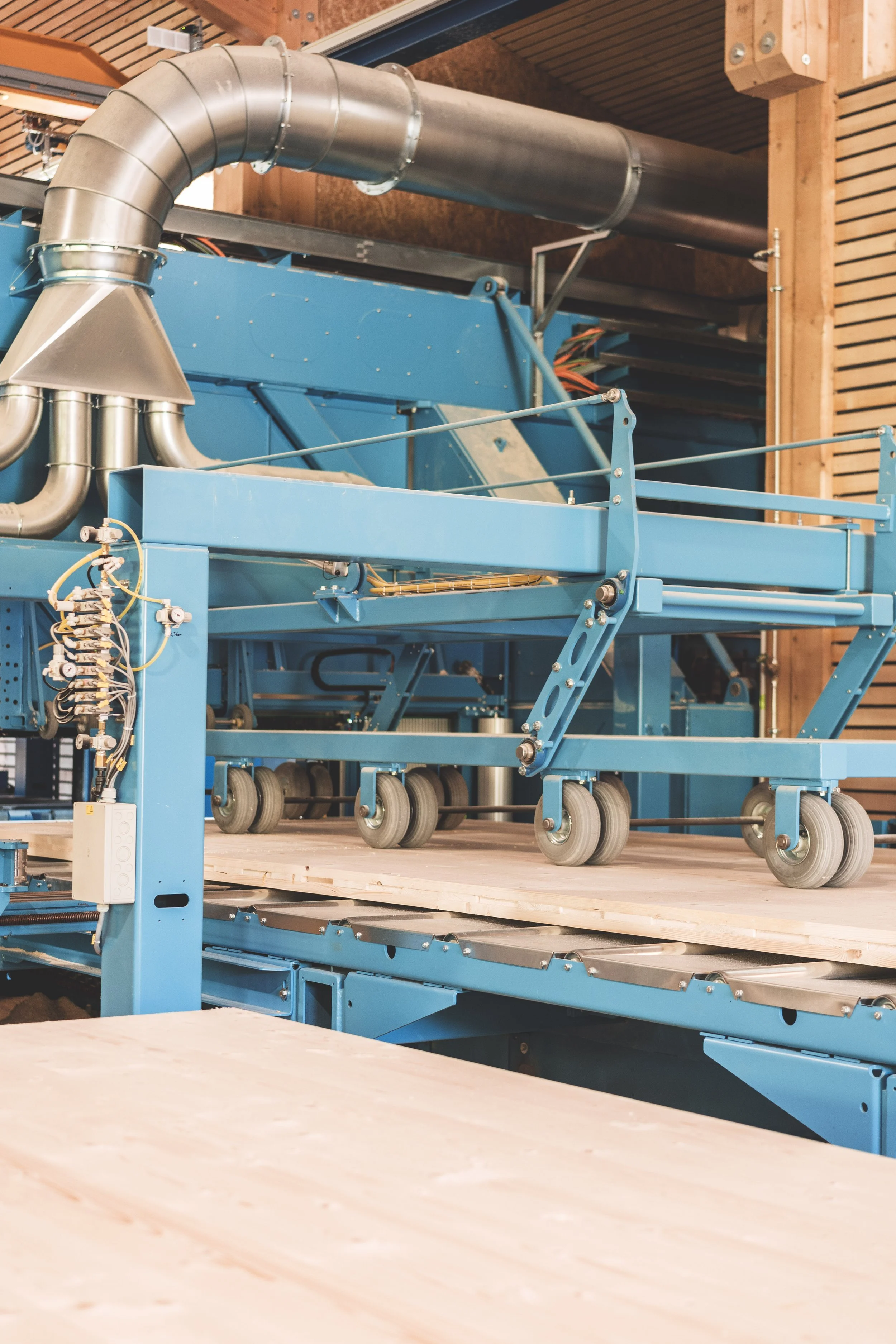 Industrielle Maschine in einer Holzwerkstatt, bestehend aus Metall und Blau, mit Rollen und Rohren, auf Holzboden