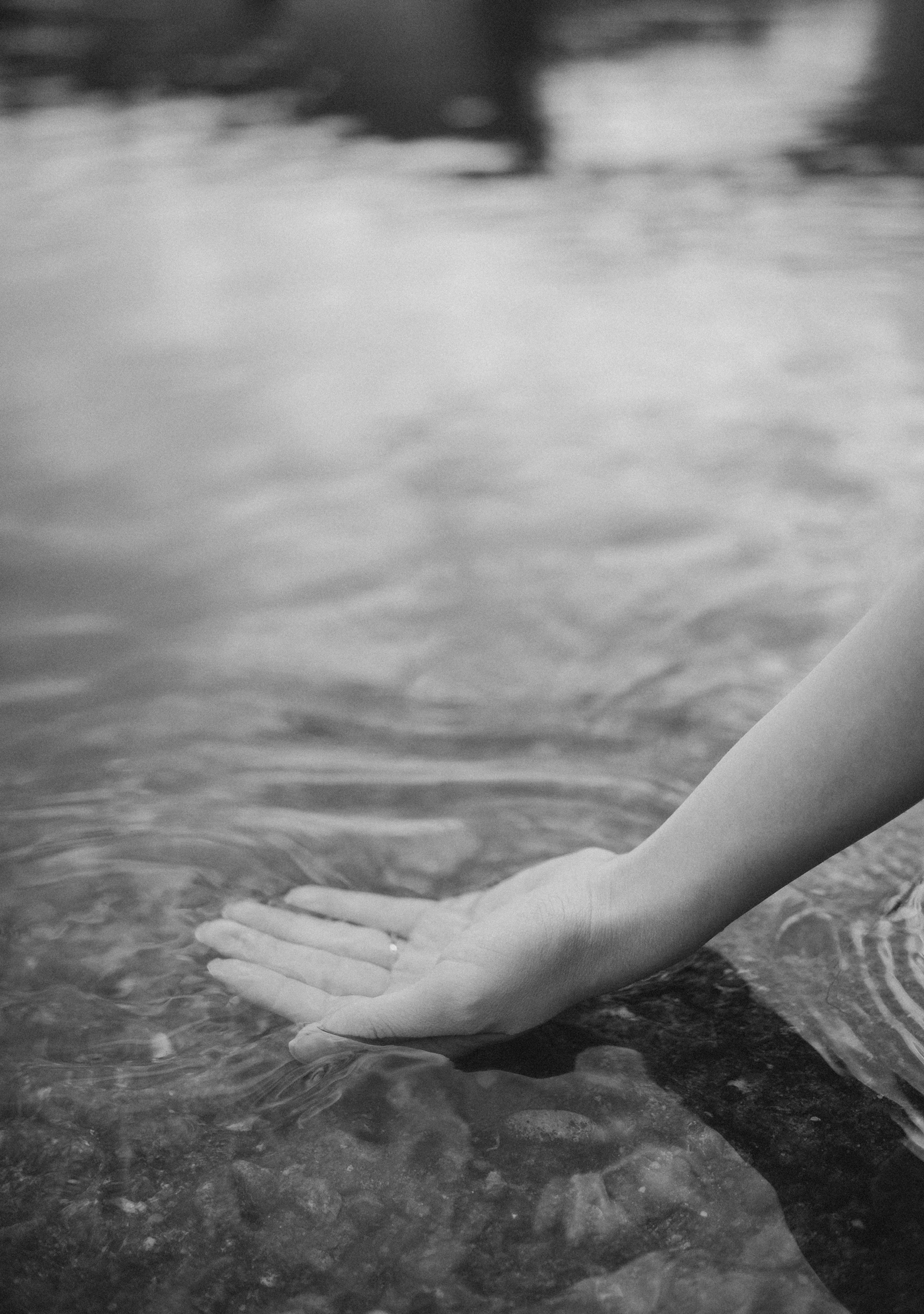 A black-and-white photo of a hand resting on water, with the water rippling around the fingers.