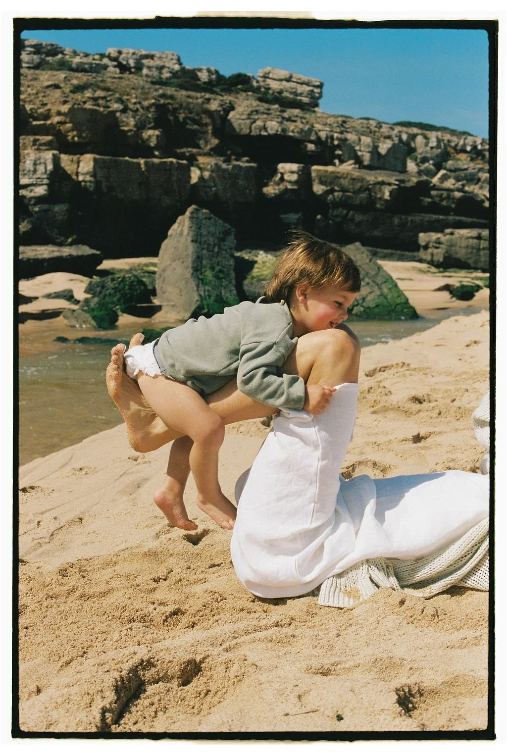 A young child riding on Keiarna from Gentle Currents back on a sandy beach, with rocky cliffs in the background.