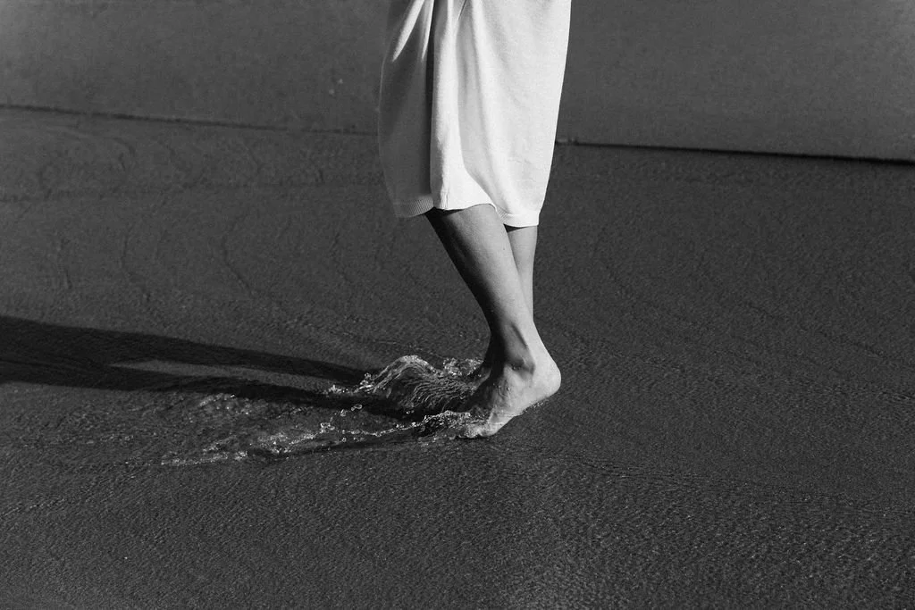 Person walking barefoot on the beach leaving footprints in the sand, black and white photo.