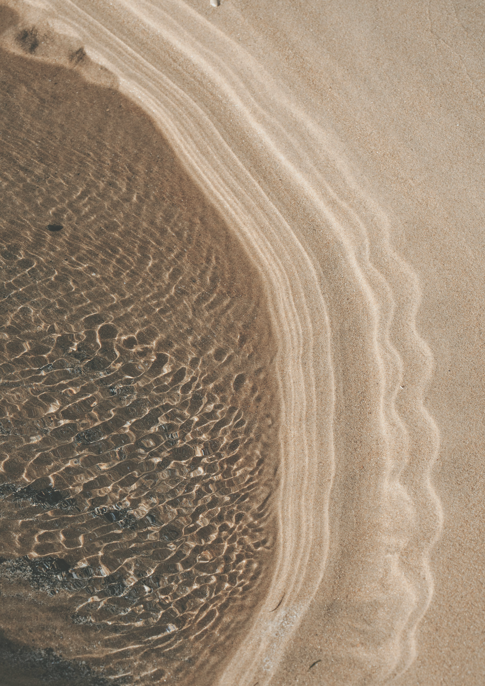 Close-up of rippling water on a sandy beach, showing patterns of waves and shallow water reflections.