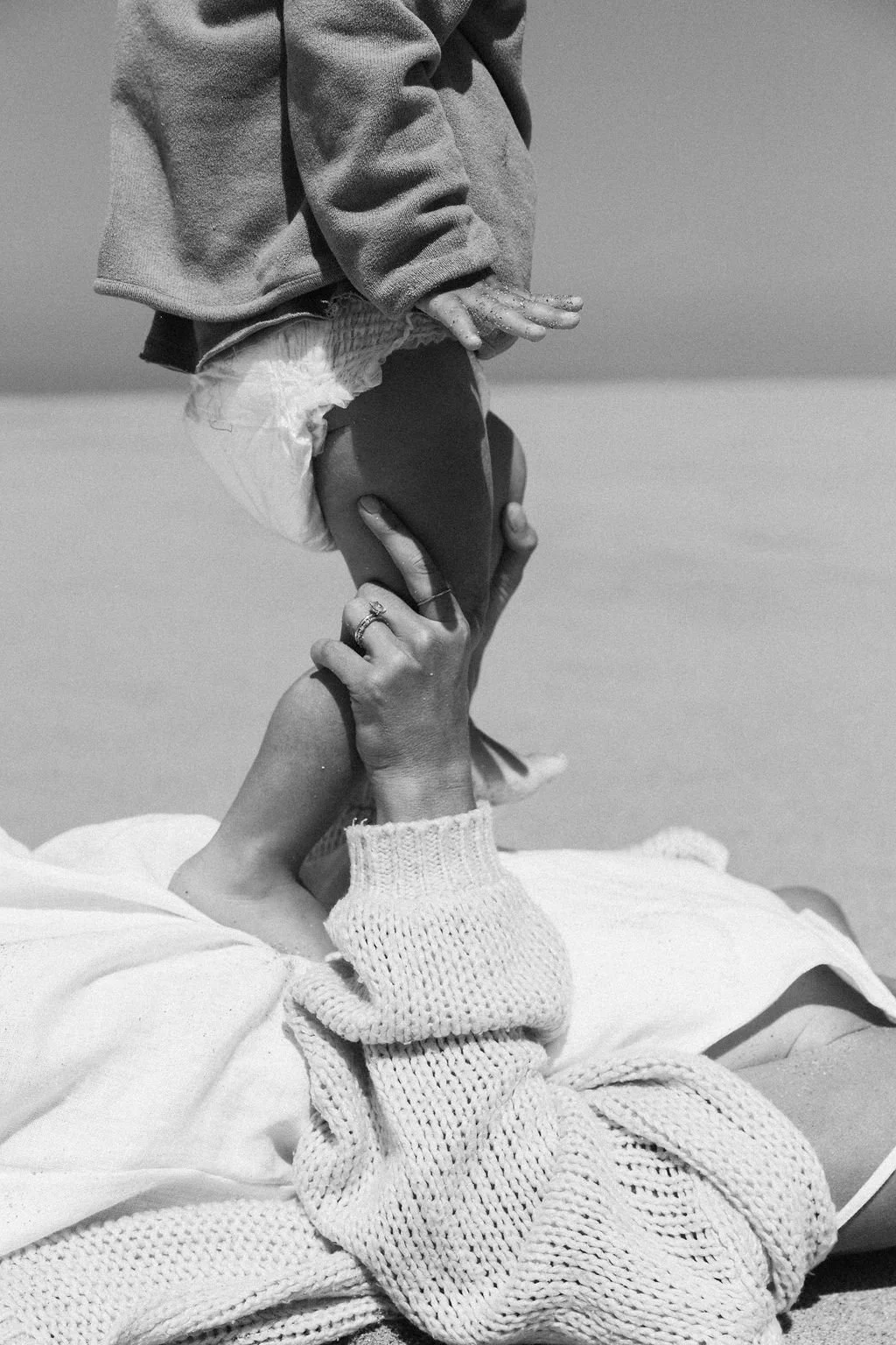 Keiarna from Gentle Currents lying on their back on the beach, with her youngest child kneeling next to them, holding their face and hand in a supportive gesture.