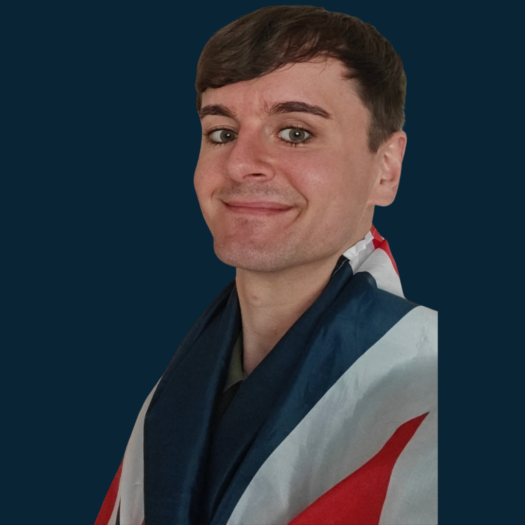 Un hombre con cabello castaño, ojos claros, sonriendo, viste una camiseta de graduación con la bandera del Reino Unido, fondo azul oscuro.