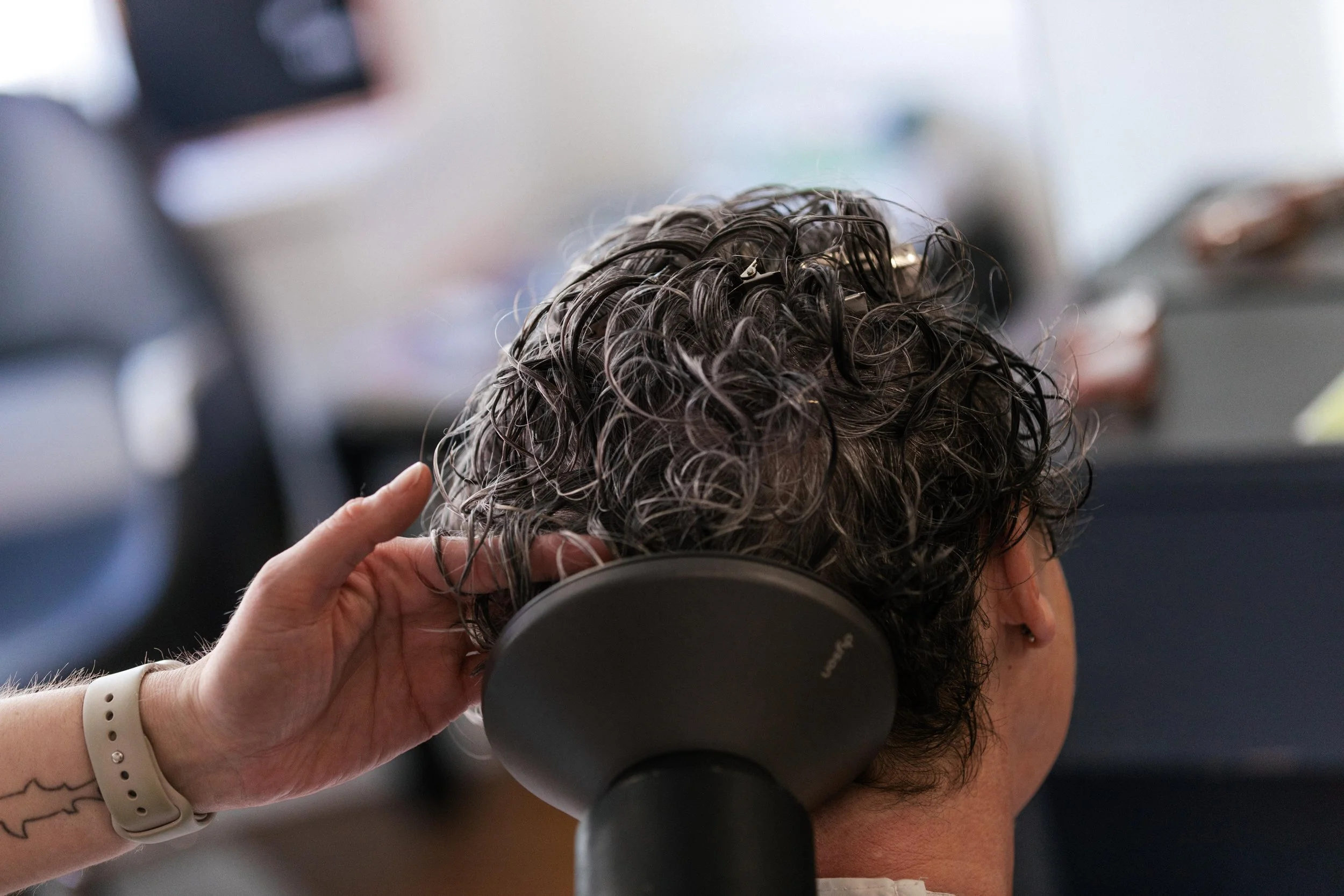 Person with curly gray hair receives ear cleaning from a professional in a salon or spa setting.