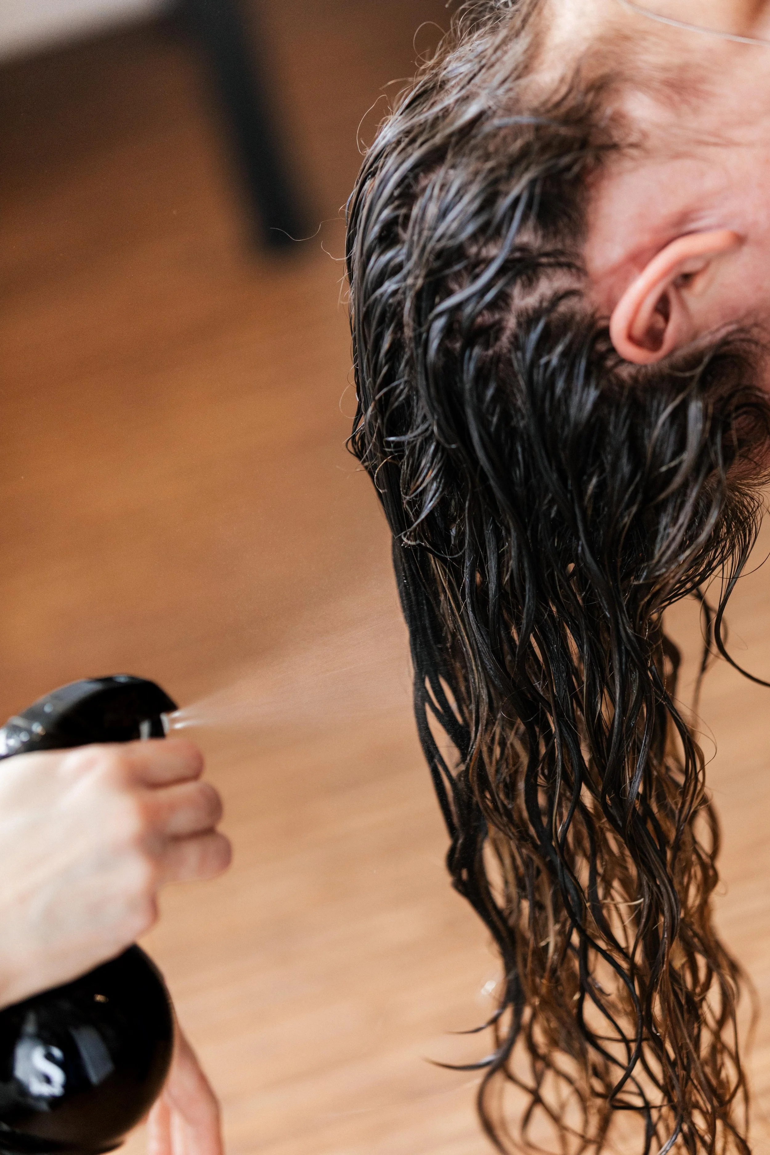 Person with long, wet hair having their hair sprayed with water, in a salon setting.