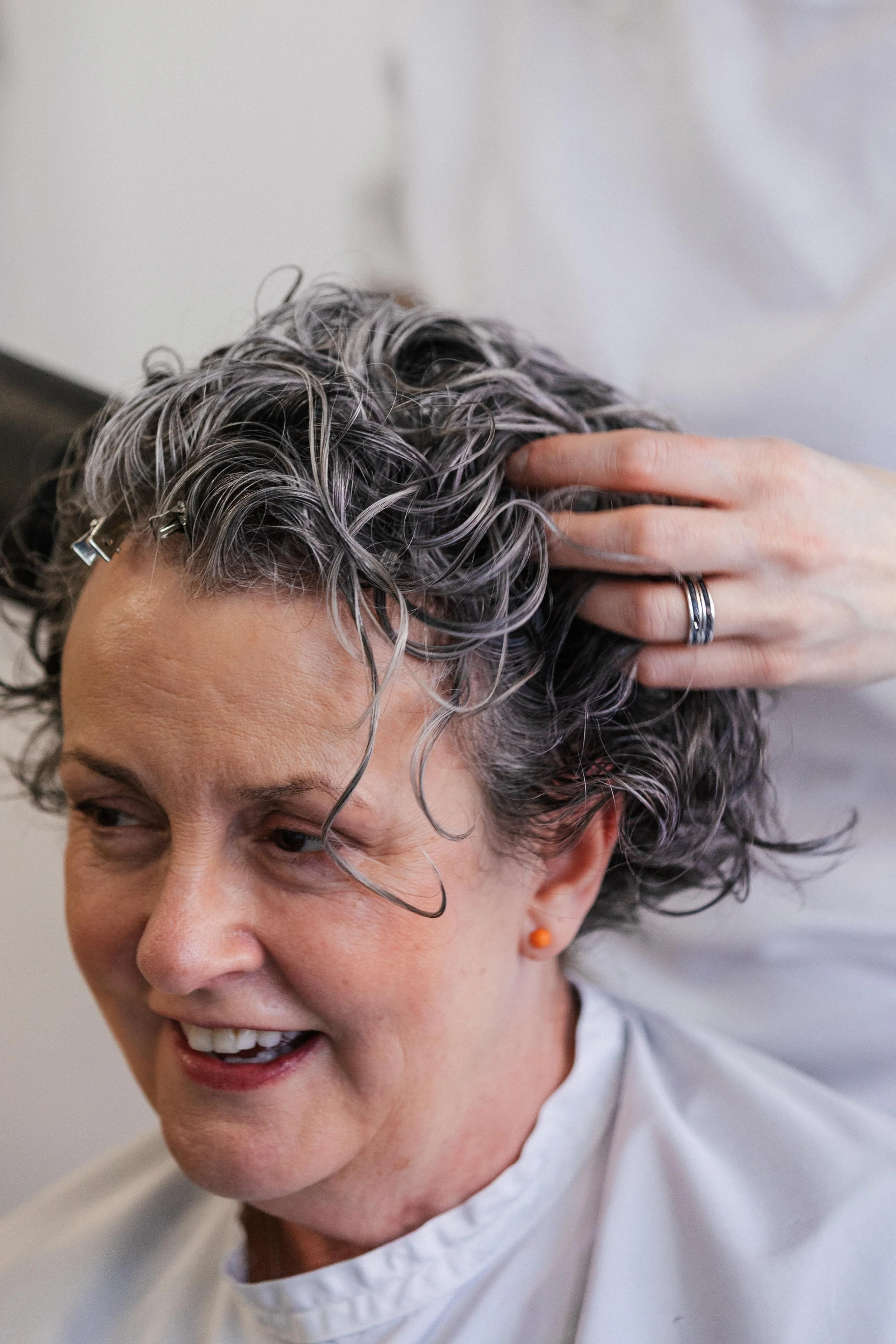 Close-up of a person with short, curly gray hair getting a haircut at a salon.