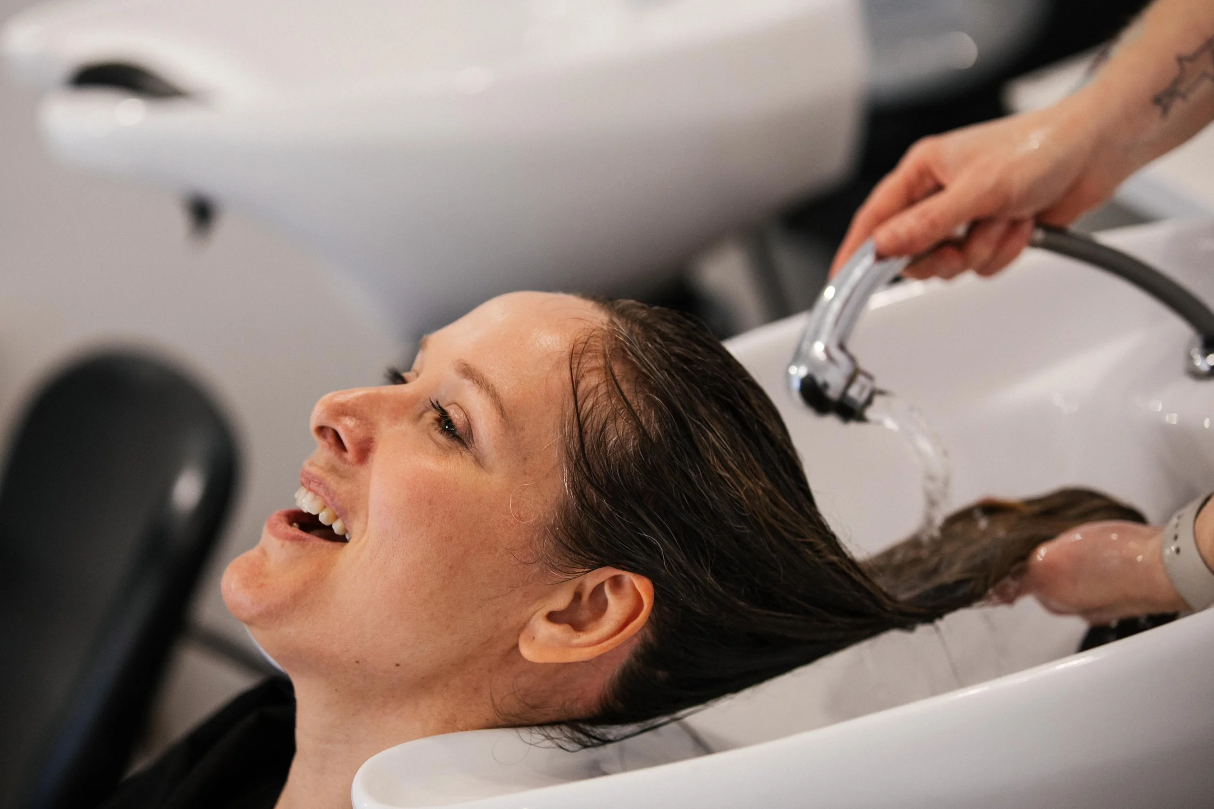 Woman with wet hair smiling while getting her hair washed at a salon hair washing station.